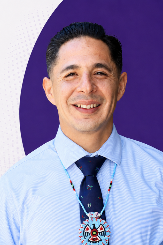 Dr. Felipe Mercado. A Mexican-American man, black groomed hair, black almond eyes, sharing a smile, wearing a blue shirt, tie, and beaded necklace of wisdom.