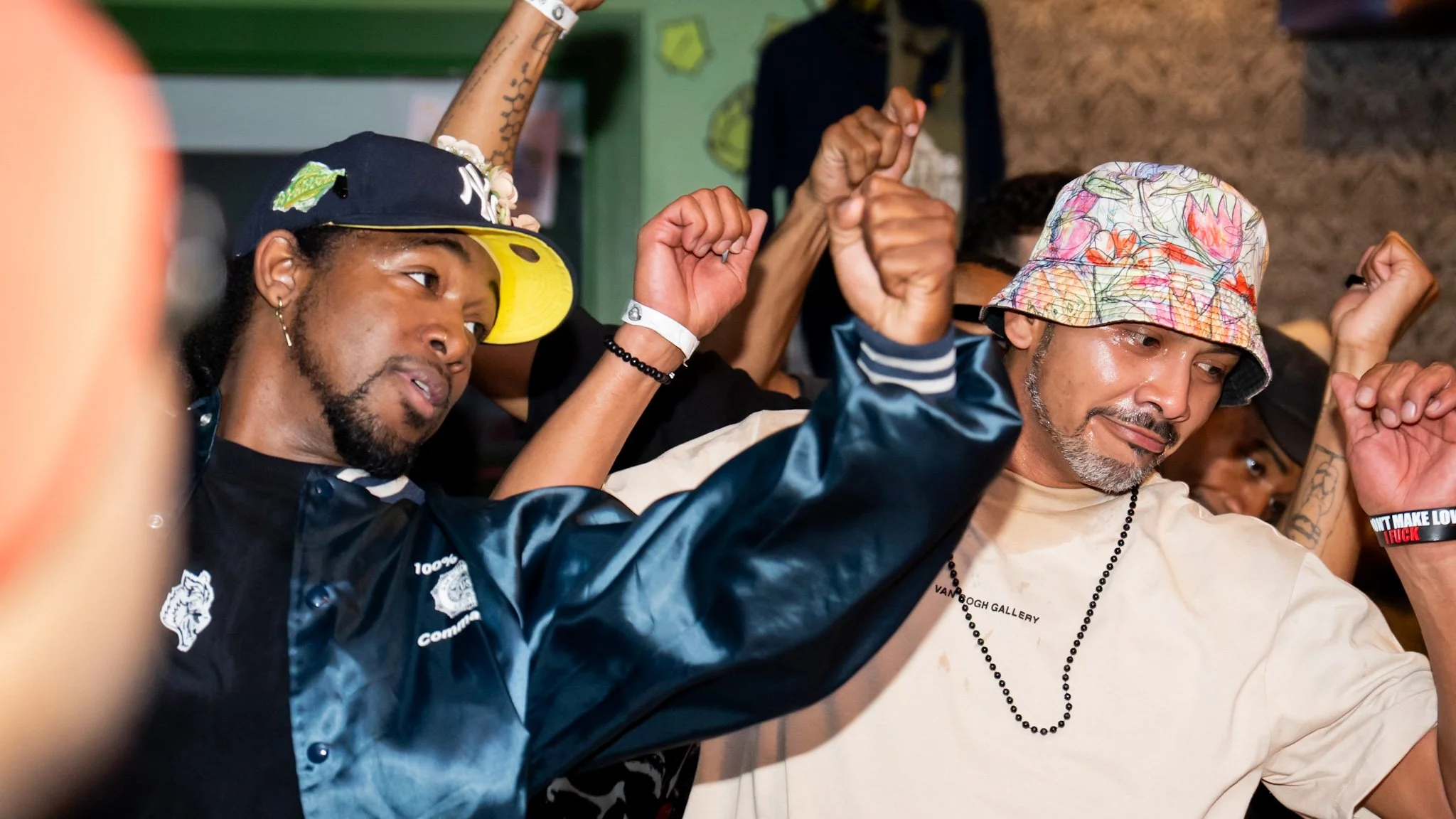 Several people, including a man with a colorful bucket hat and a man with a baseball cap, are raising their fists in a celebratory gesture. They appear to be enjoying an event or gathering.