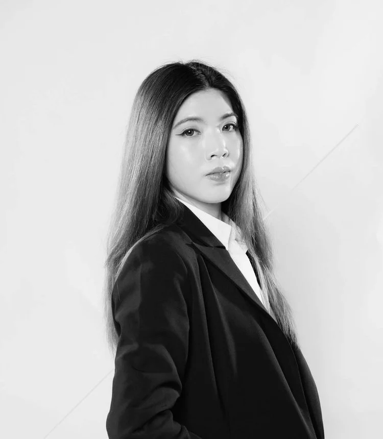 Black-and-white portrait of a woman with long straight hair, wearing a blazer over a shirt, looking at the camera with a confident expression.