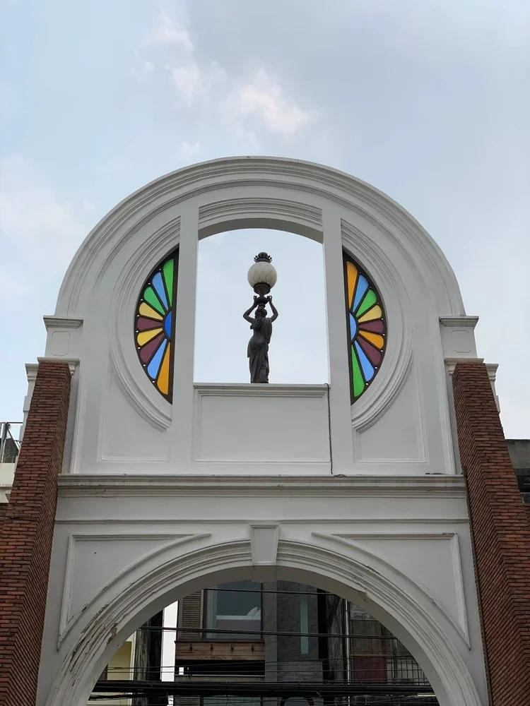 Archway with a sculpture of a woman holding a lamp at the top, stained glass windows on either side, and brick columns.