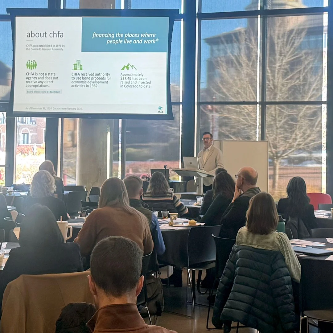 Conference attendees sitting at a table and a speaker at the podium with slides being shown off to the side