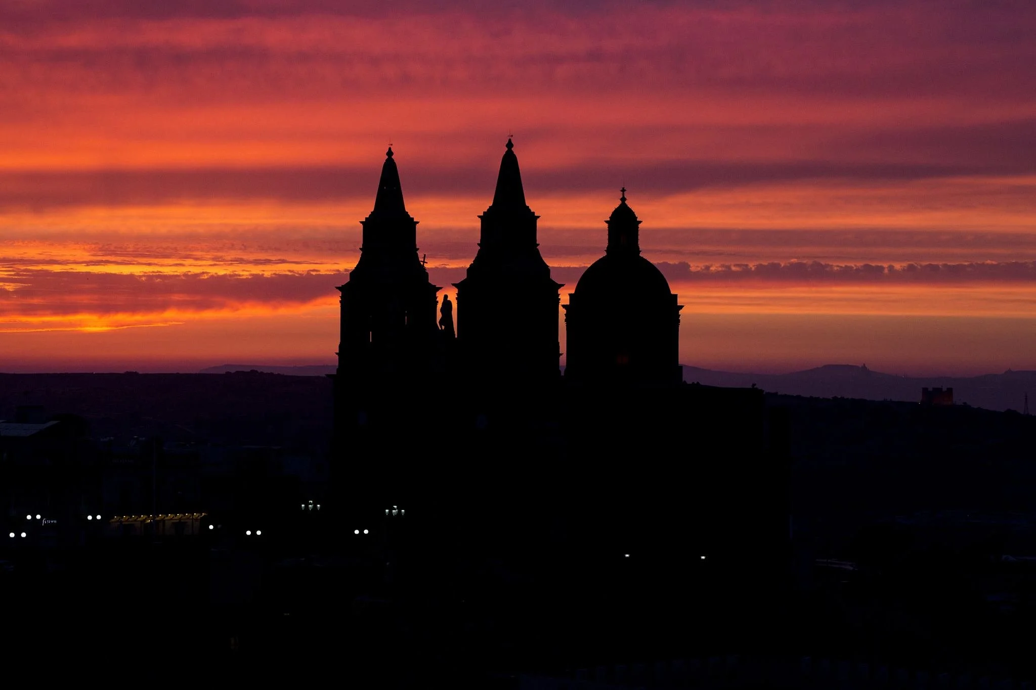 Silhouette of a historic church with three spires against a colorful sunset sky with purple, orange, and pink hues.