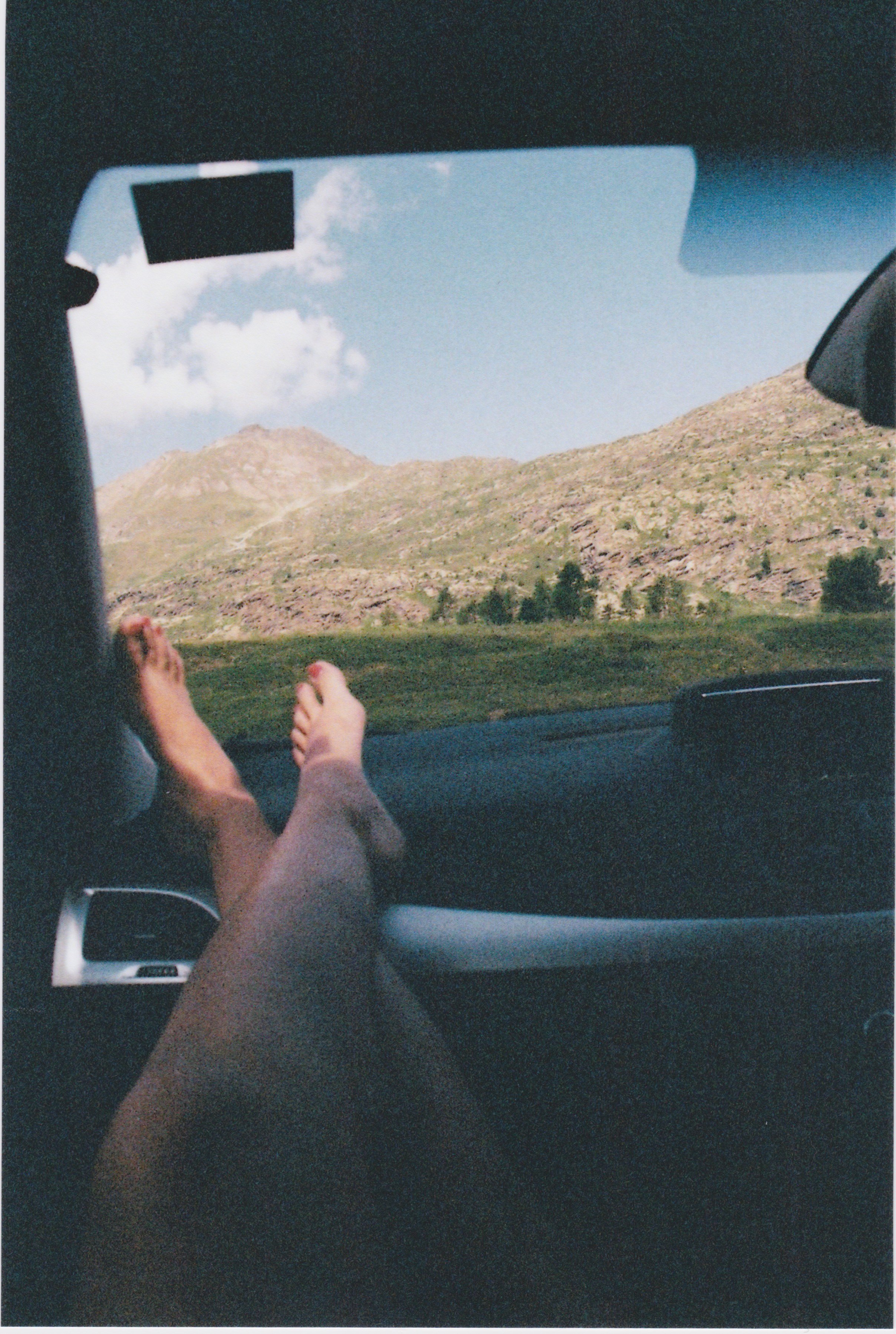 View from inside a car of a person resting their feet on the dashboard, with a mountainous landscape visible through the windshield.