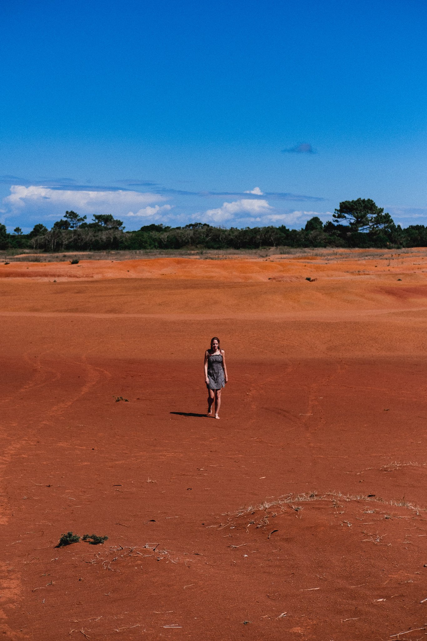 Woman walking on a red sandy landscape under a clear blue sky.