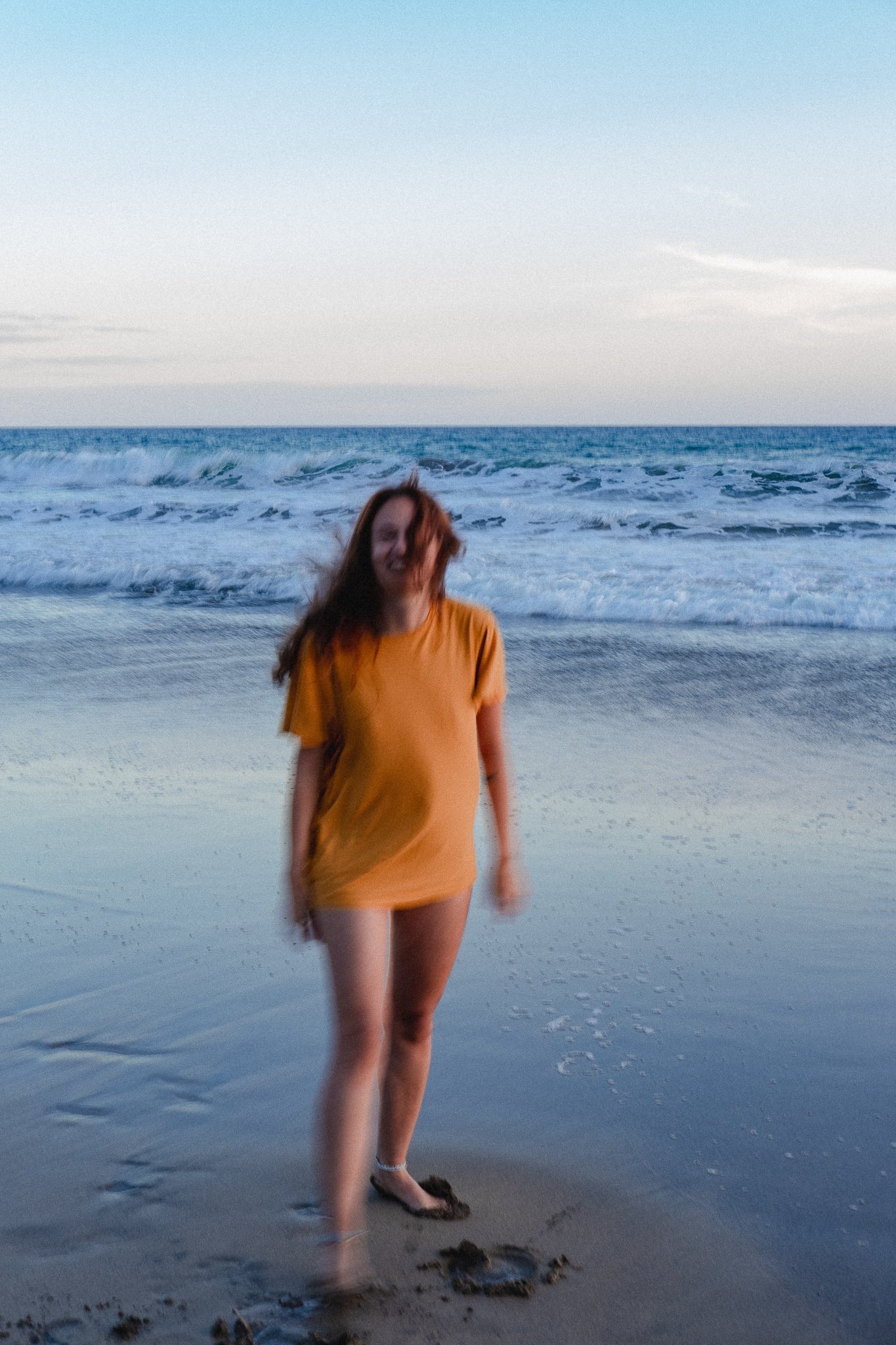 Blurry image of a person in a yellow dress walking on a beach with waves in the background.