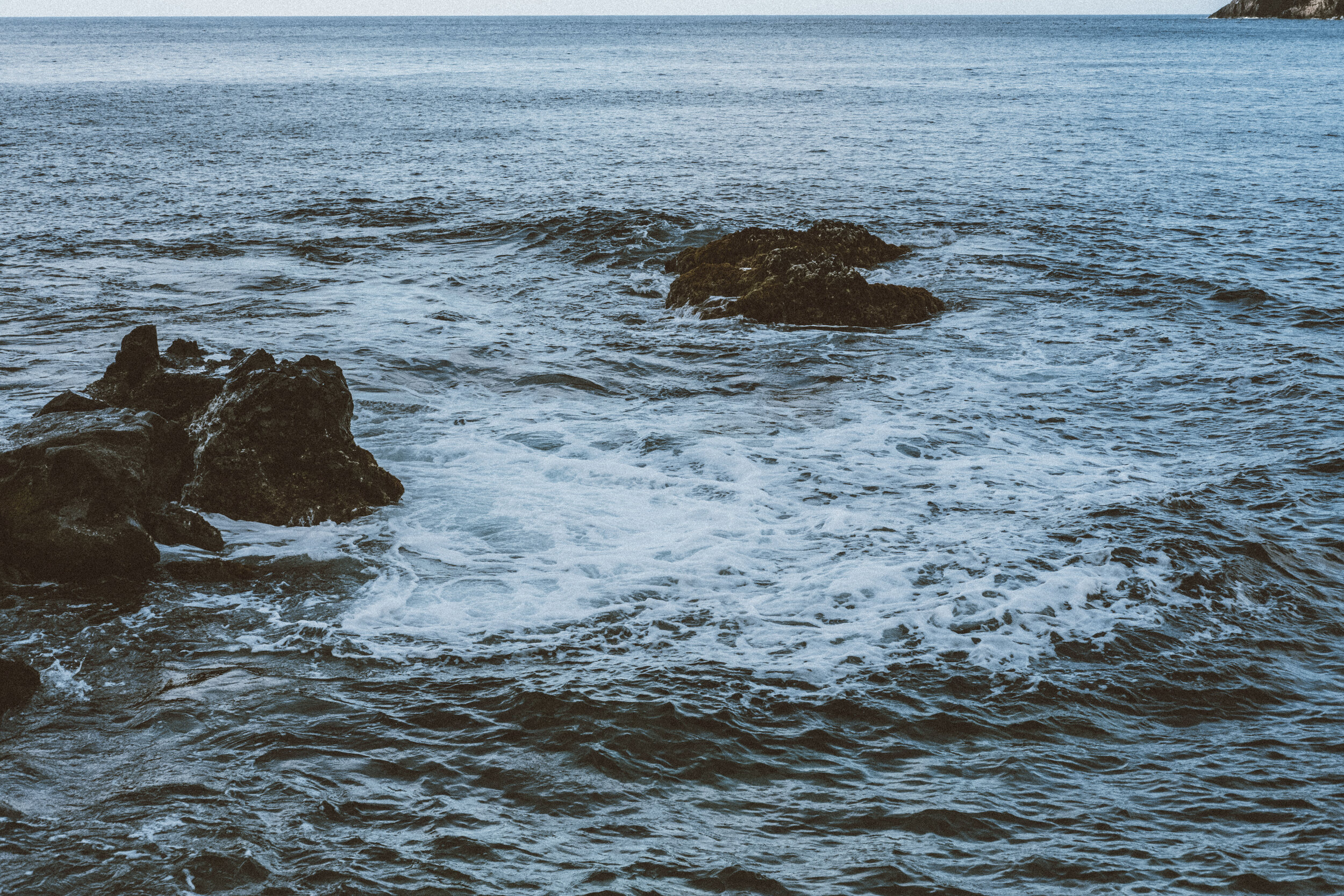 Ocean waves crashing against rocks with a horizon view.