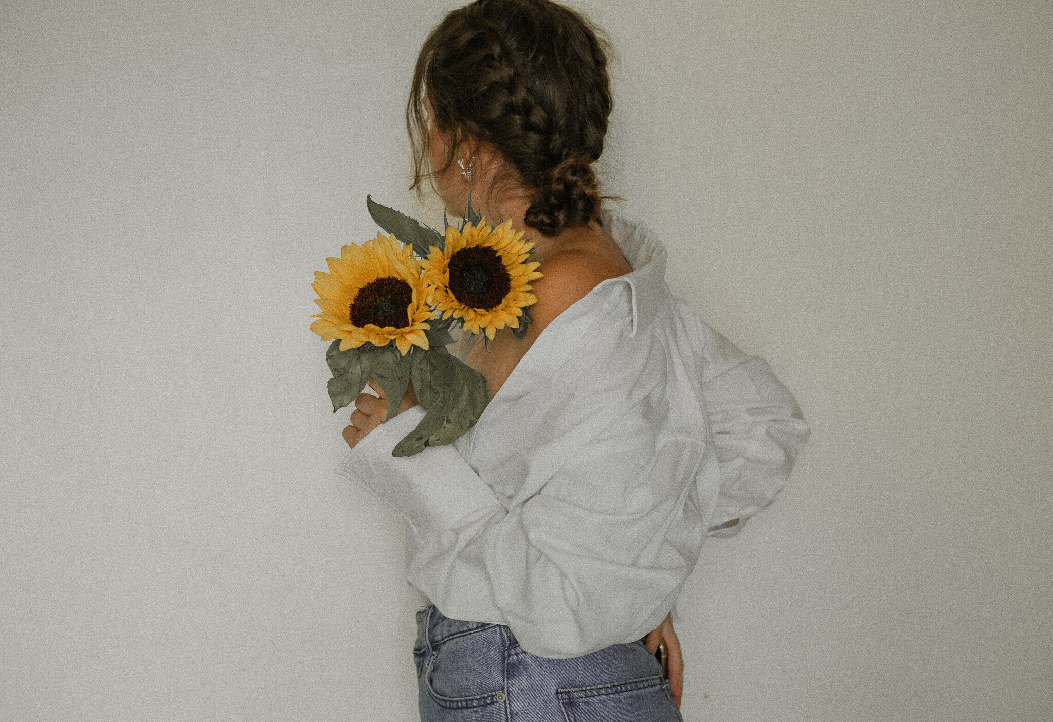 Person with braided hair and white shirt holding sunflowers