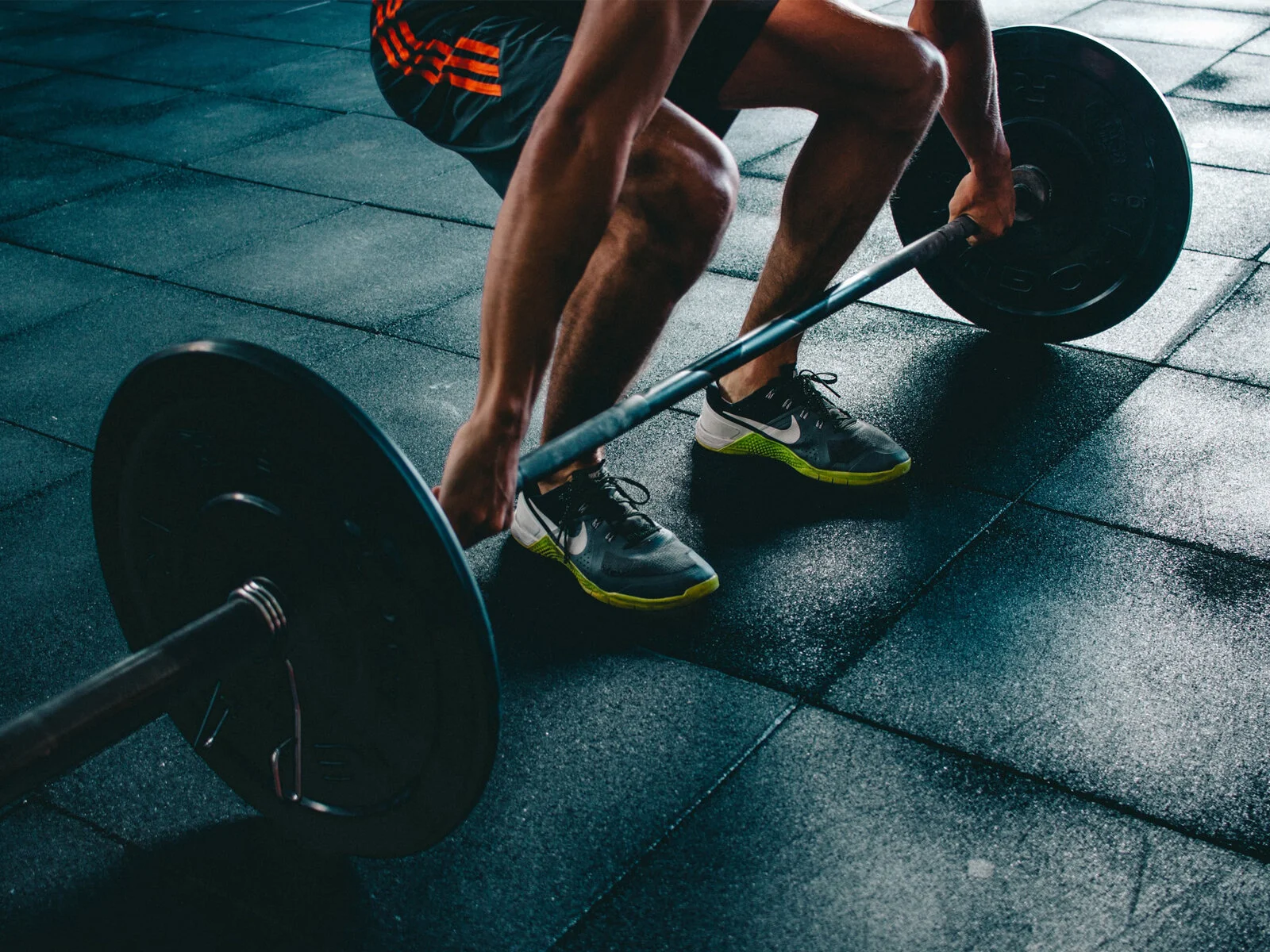 A person lifting a barbell with weights during a workout in a gym with rubber flooring.