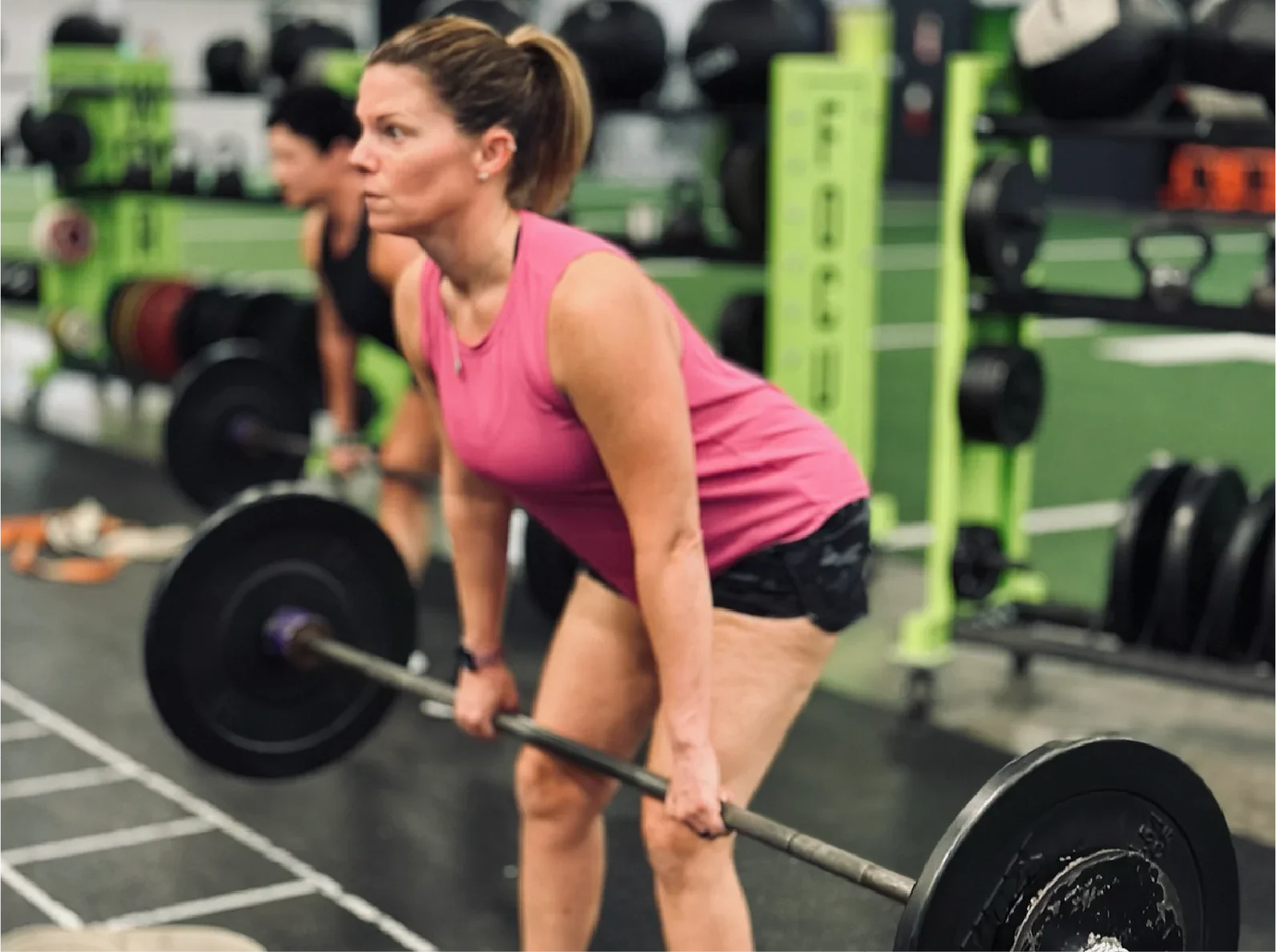 Mom performing barbell deadlift during coached small group workout