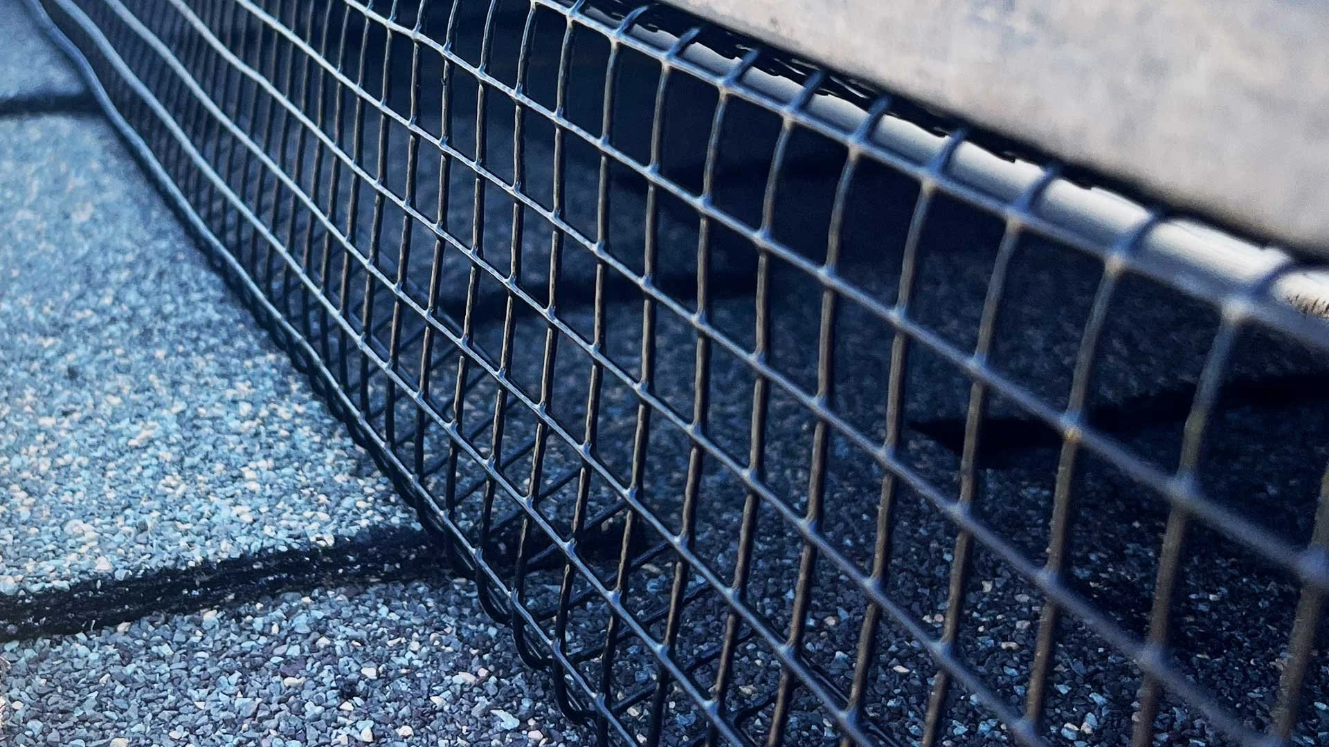 Close-up of a black metal wire fence on a gravel surface