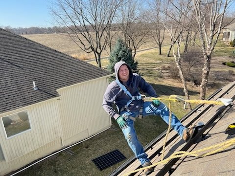 a man on a roof wearing a harness and a dark hoodie while installing solar
