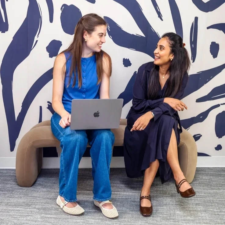 Two Women chatting on a bench in front of a bold navy and white abstract painted wall.