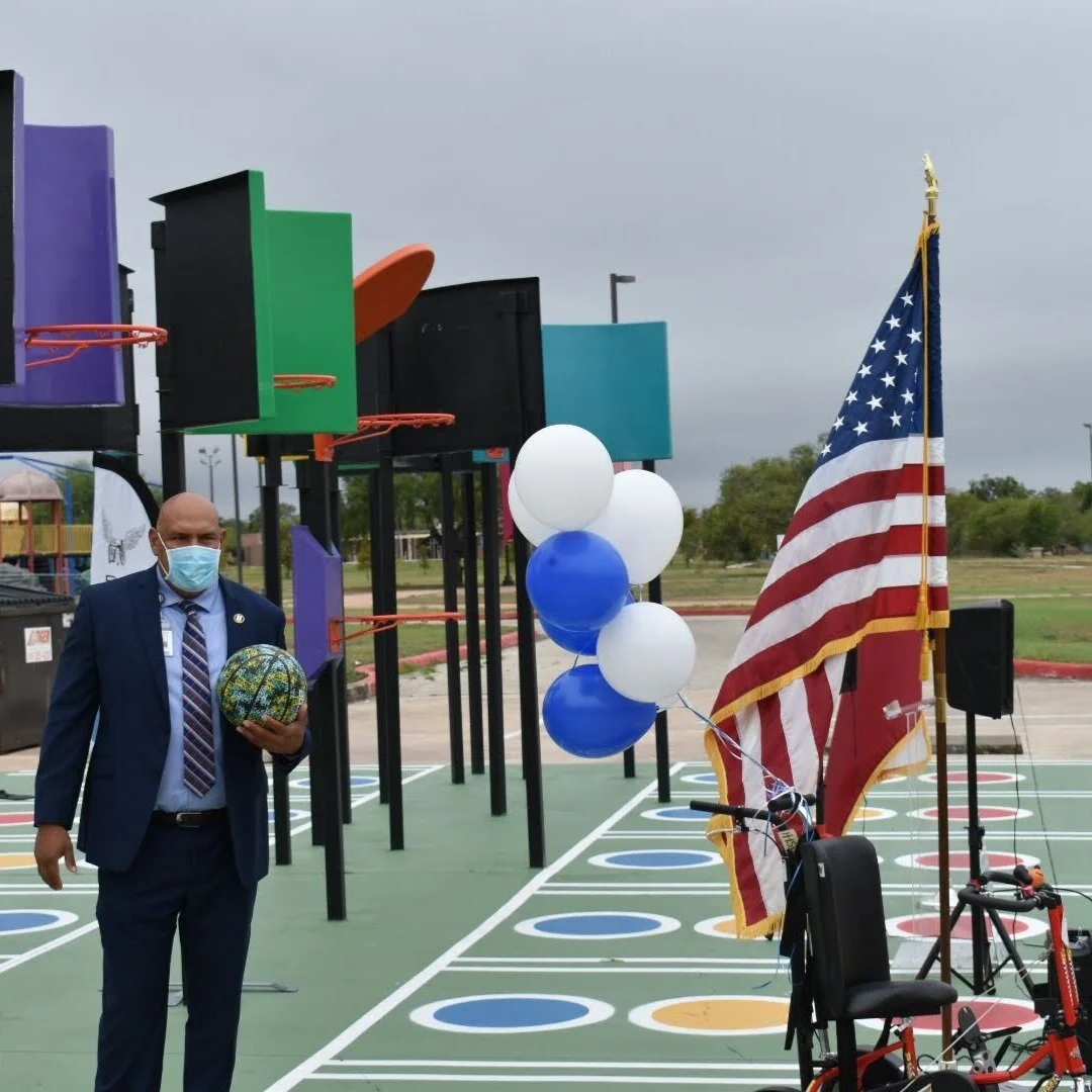 An outdoor, universally accessible playground featuring multiple non-traditional basketball hoops with uniquely shaped, colorful backboards.