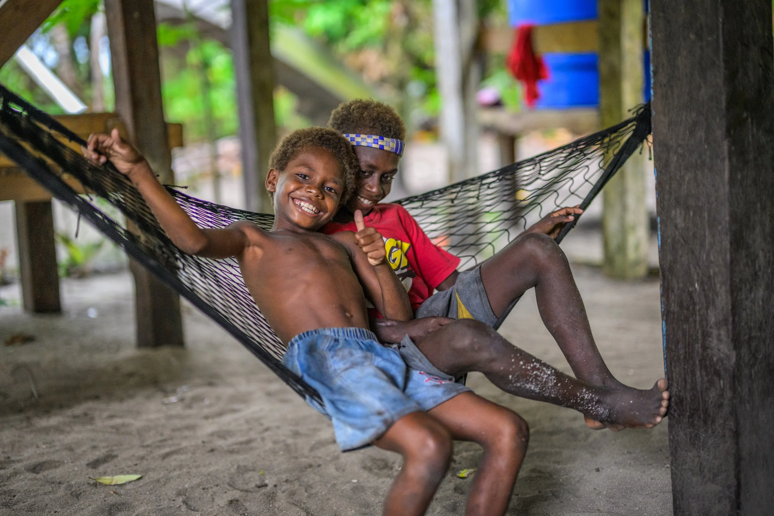 Two children pose in a hammock in a local community on Tunnung Island, Lovongai LLG, New Ireland Province, Papua New Guinea.