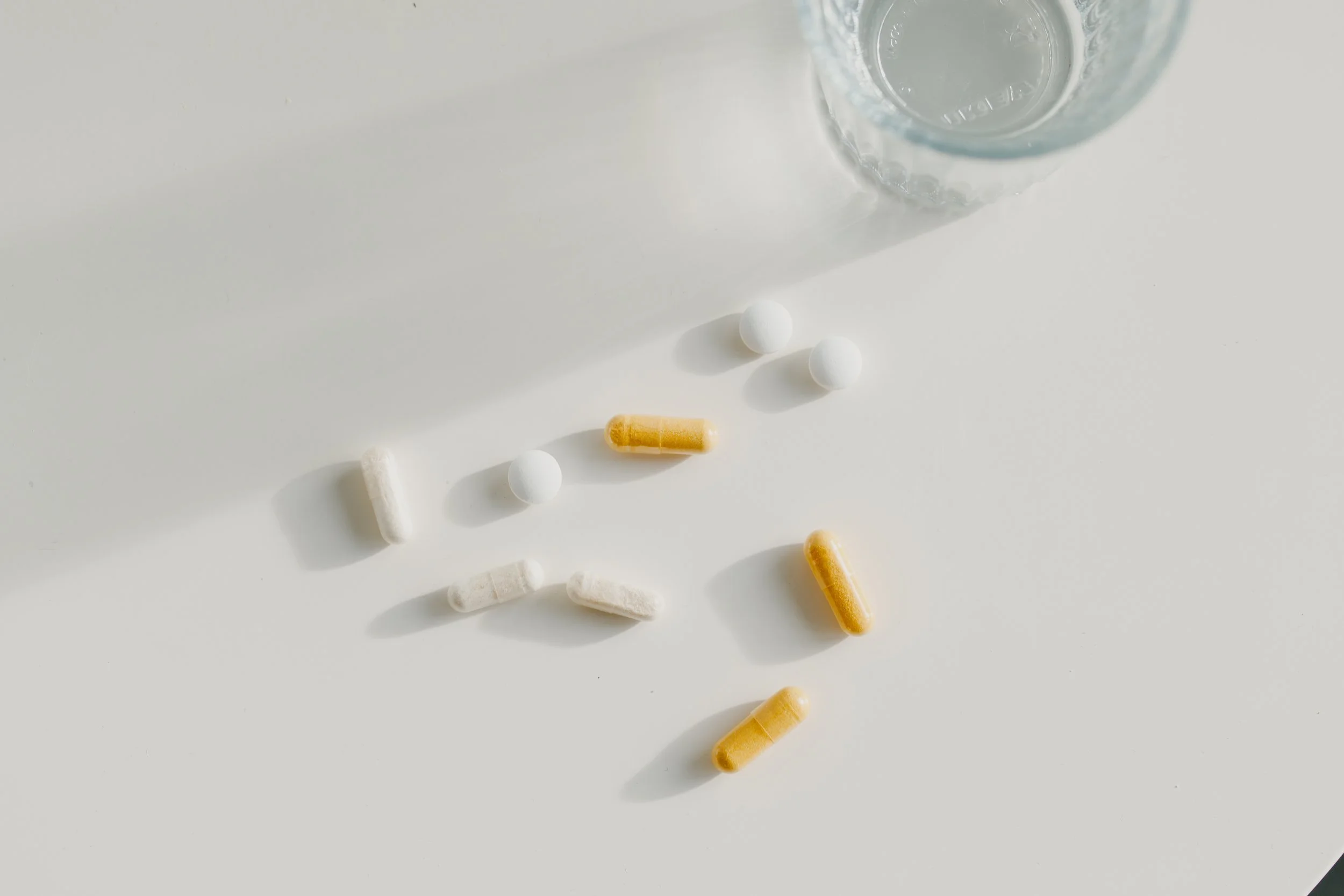 Pills, capsules, and a glass of water on a light surface for Tandem Clinic’s Cardio-Metabolic Health visit.