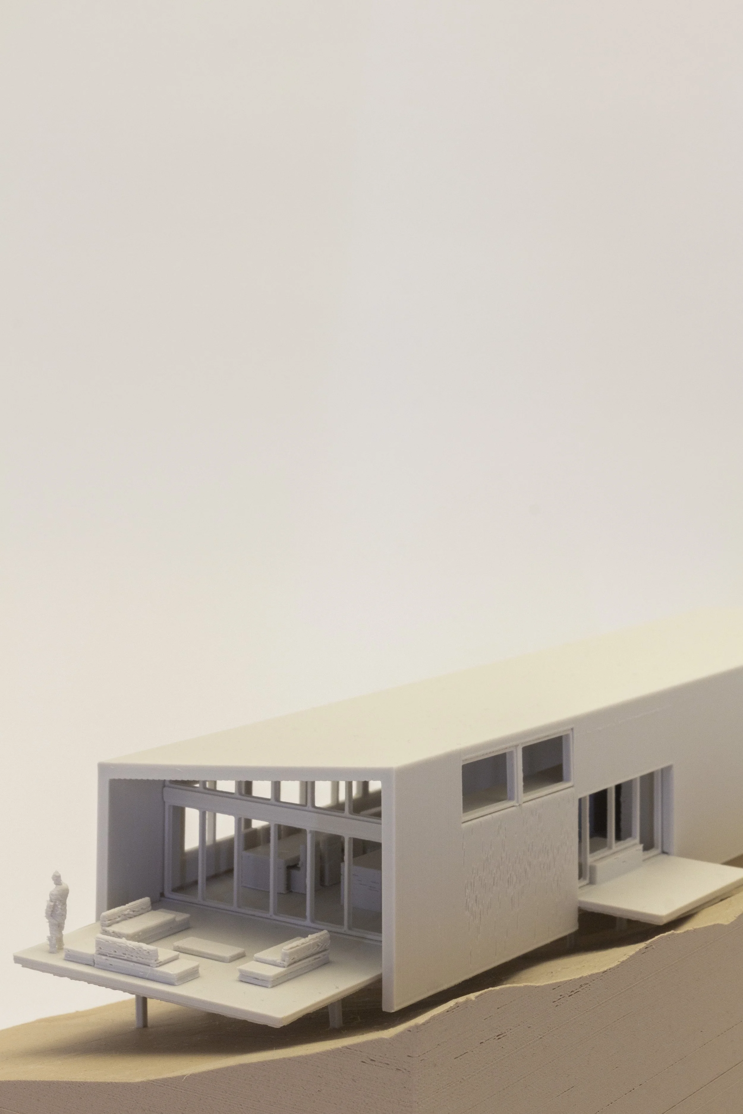 Architectural study model of a small house with a deep roof overhang and glazed living space opening to a terrace.