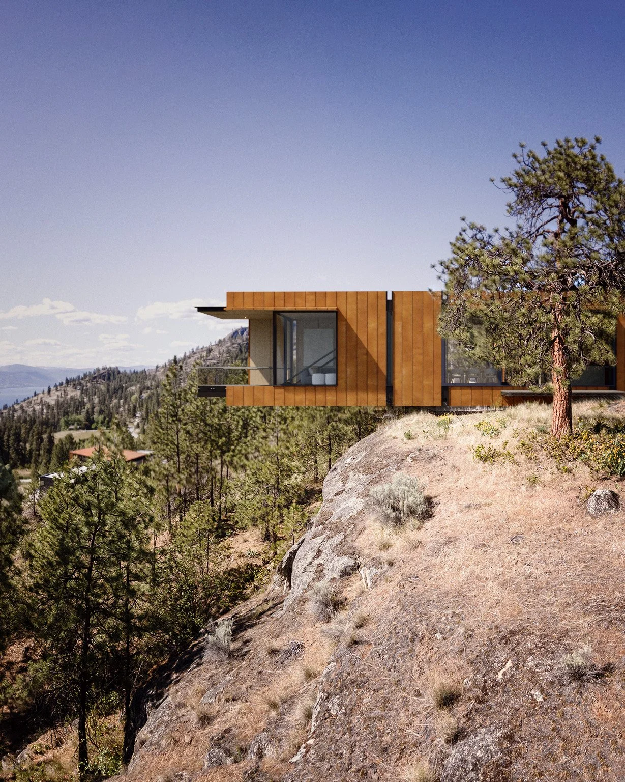 Daytime view of a weathering steel-clad house cantilevering from a rocky ridge above Okanagan Lake in Naramata.