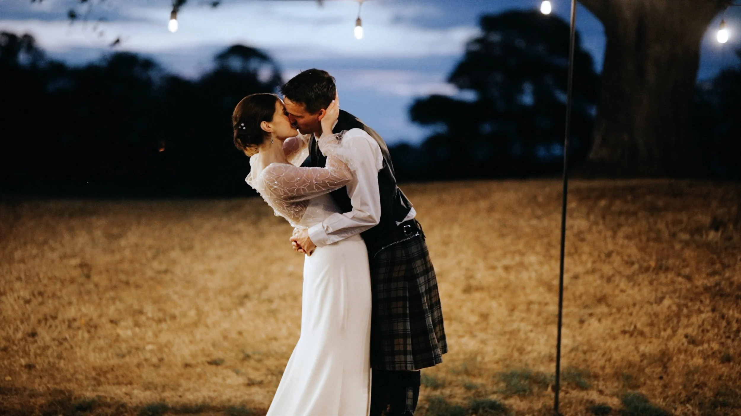 Paul and Laura sharing a kiss beneath festoon lights