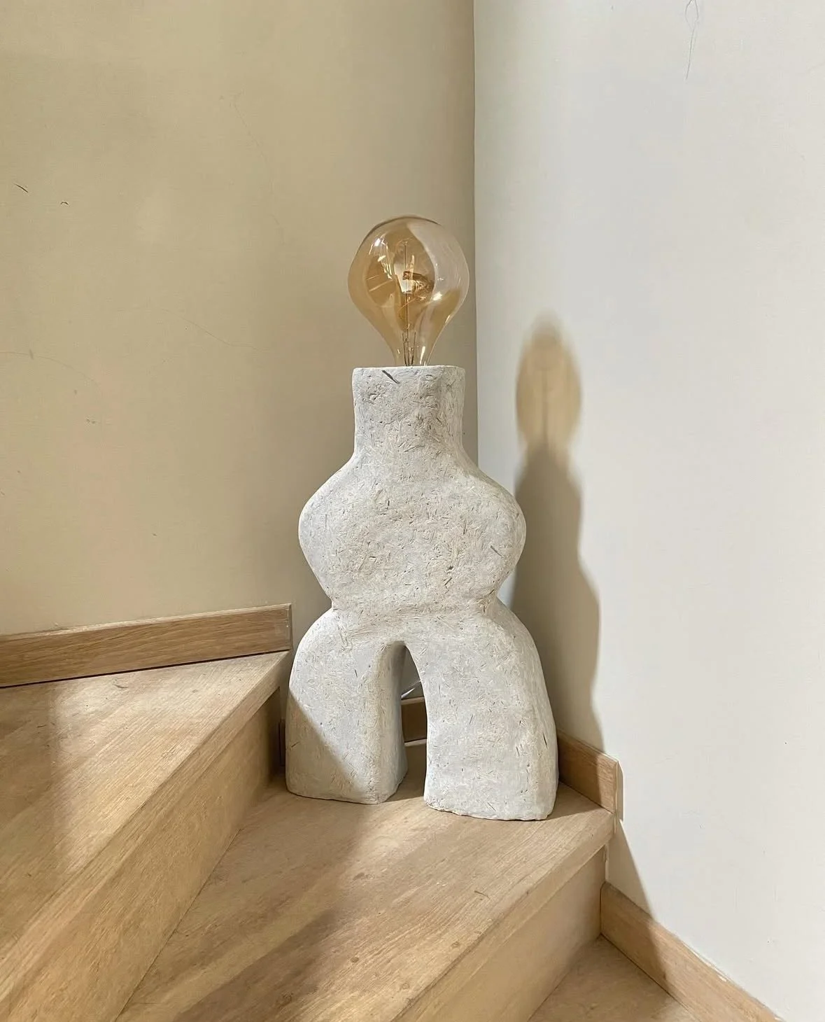 Lámpara de mesa fabricada con hormigon de cañamo, en forma abstracta y bombilla de filamento visible