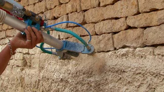 Mano con equipo de proyeccion de hormigon de cañamo, en una pared de piedra