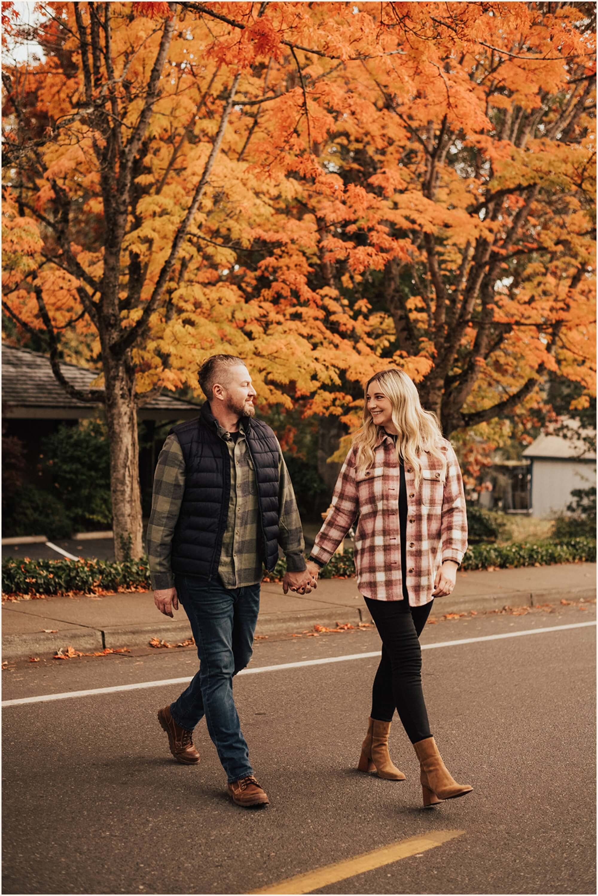 Couple holding hands while walking across street with fall foliage in background