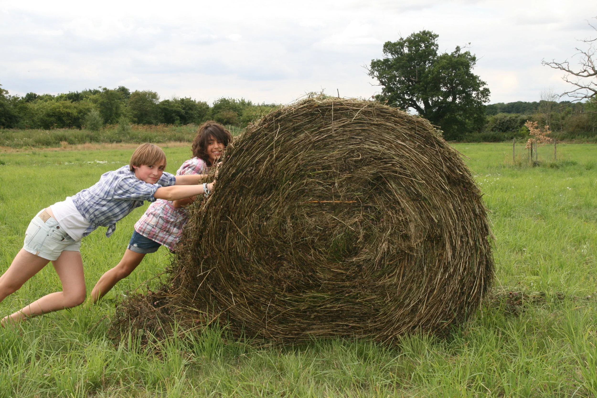 Two girls rolling a bail of hay