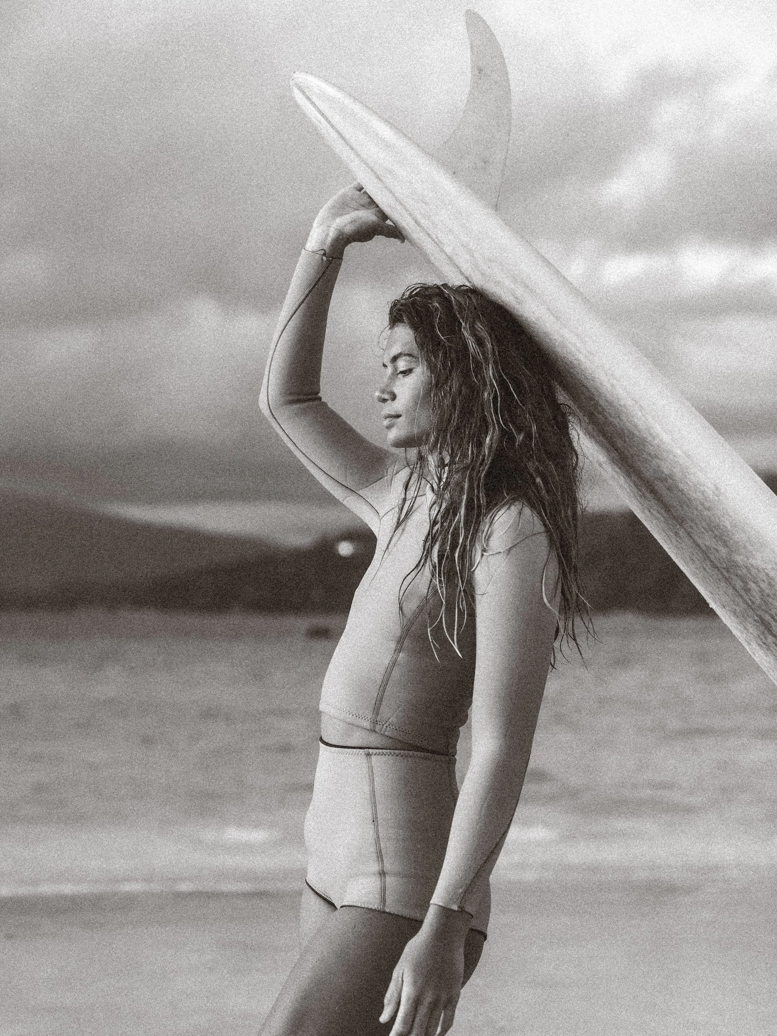 Model and Professional Roxy Longboard Surfer, Vaimiti, holding a surfboard on top of her head while wearing an Abysse Wetsuit for a fashion and brand photoshoot in Tahiti, French Polynesia with photographer, Lynsey Garfinkel and Warm Collective