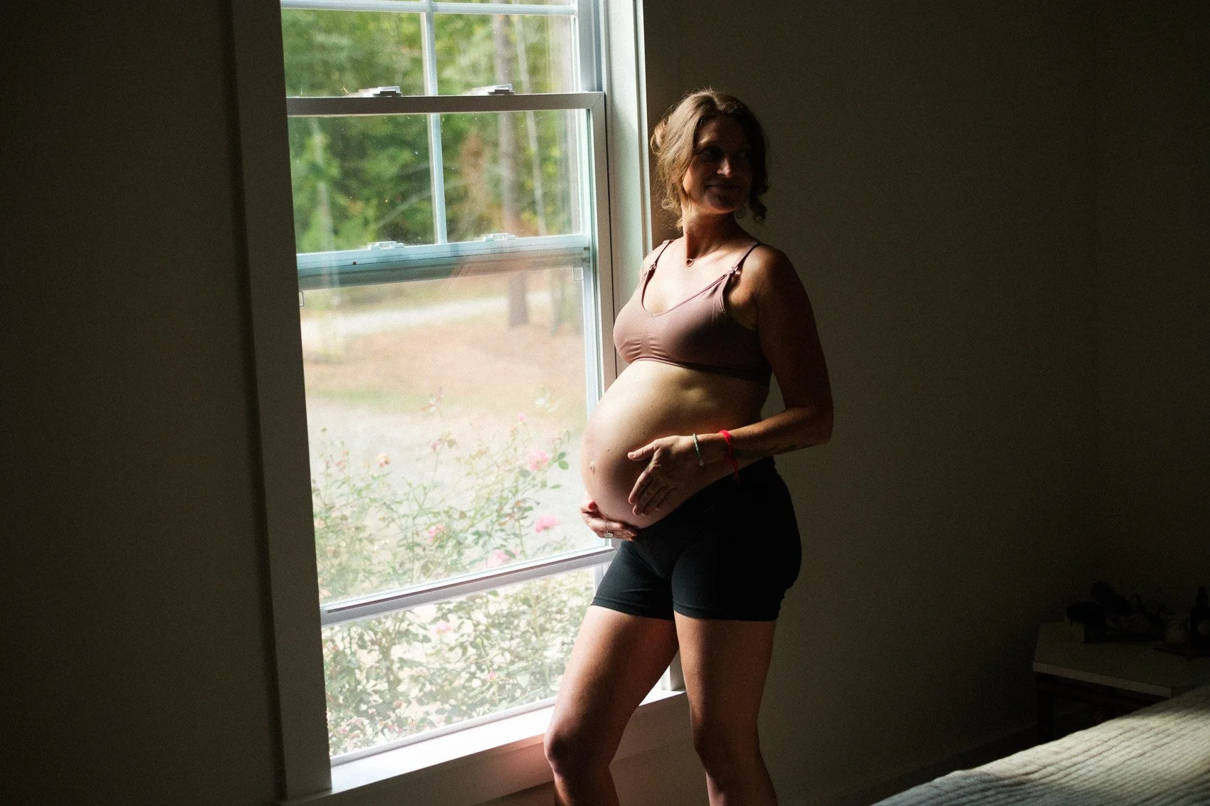 pregnant mom standing in window and looking over shoulder
