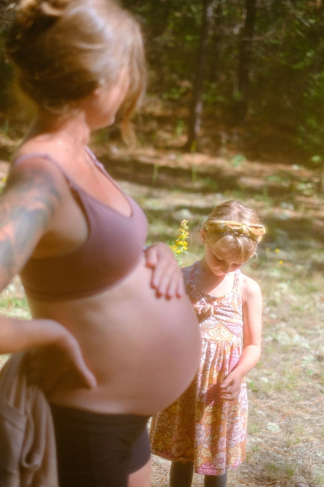 Pregnant mom with hand on belly, big sister standing just behind