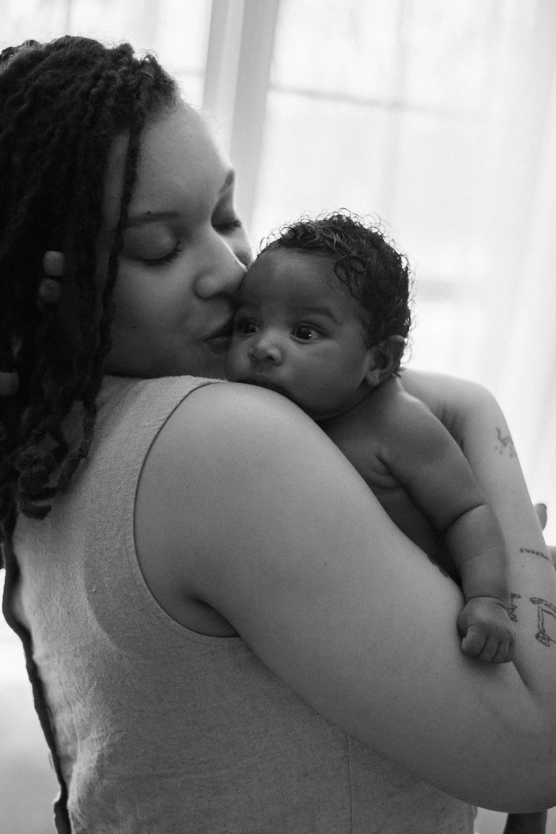Mother kissing baby's cheek in front of window in black and white