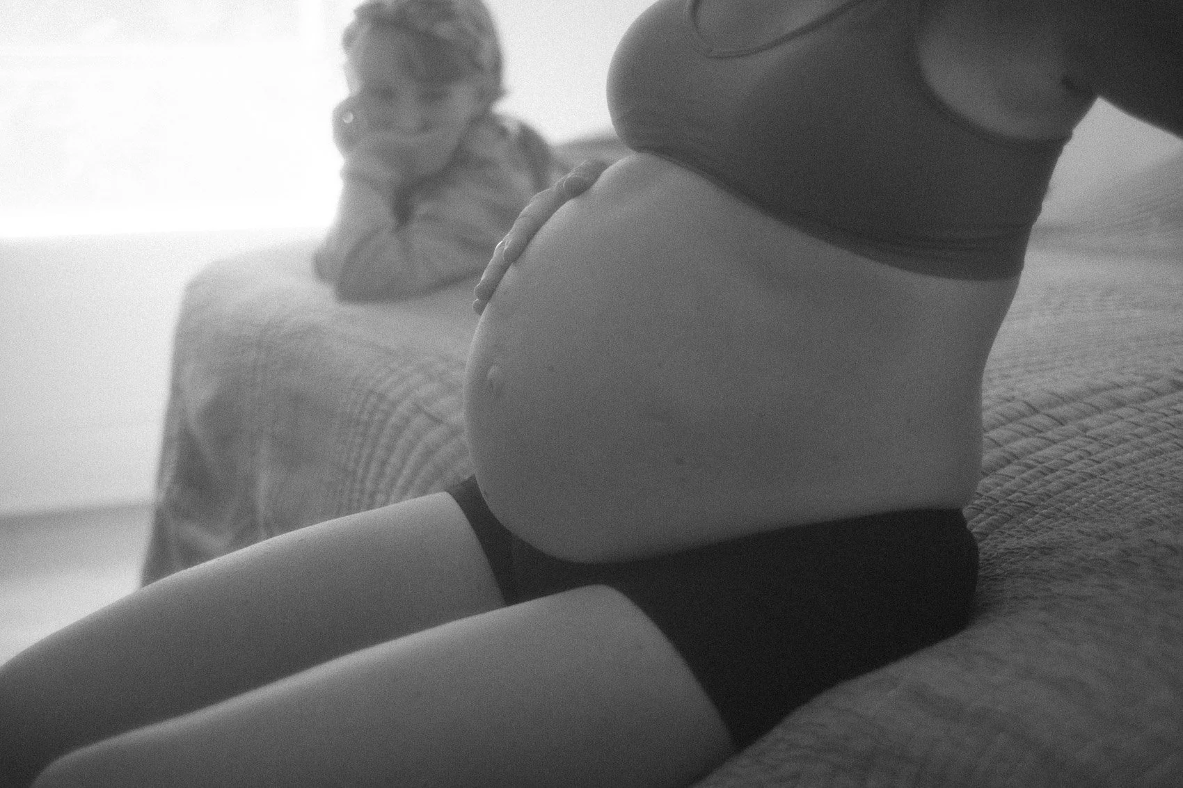 close up black and white photo of pregnant belly and big sister looking on