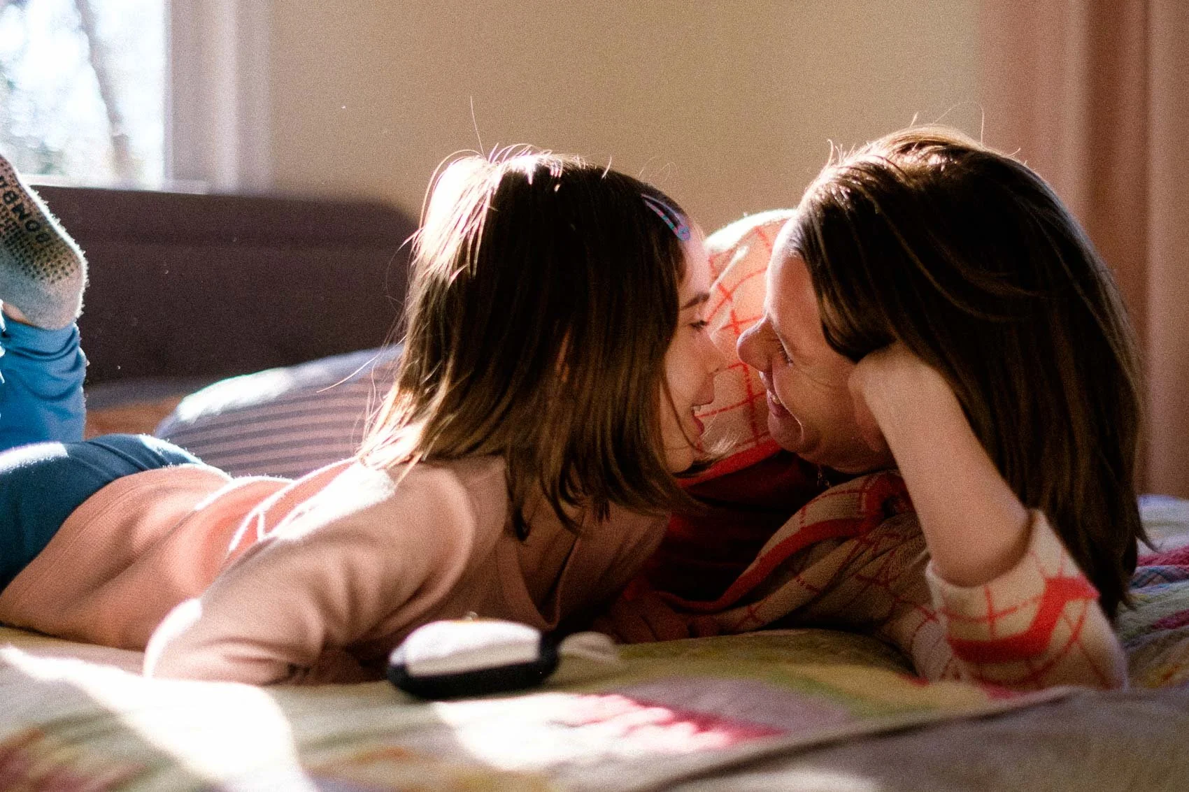 mom and daughter on bed nuzzling noses