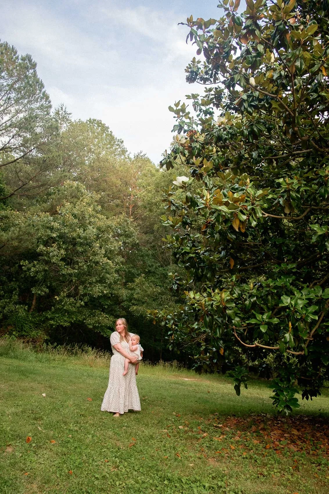 Mom and baby standing beneath a magnolia tree