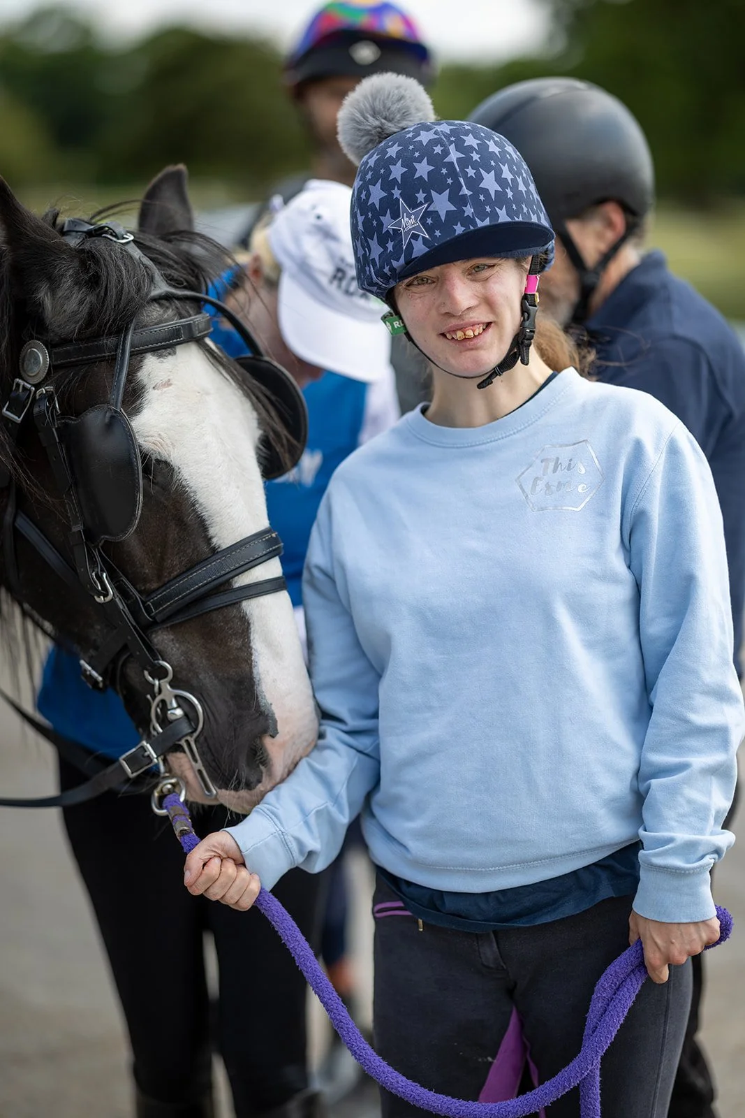 A woman wearing a Queen Elizabeth II themed hat and sunglasses standing next to a large banner with an image of Queen Elizabeth II, celebrating her Platinum Jubilee. The banner features the British flag colors and official emblems.
