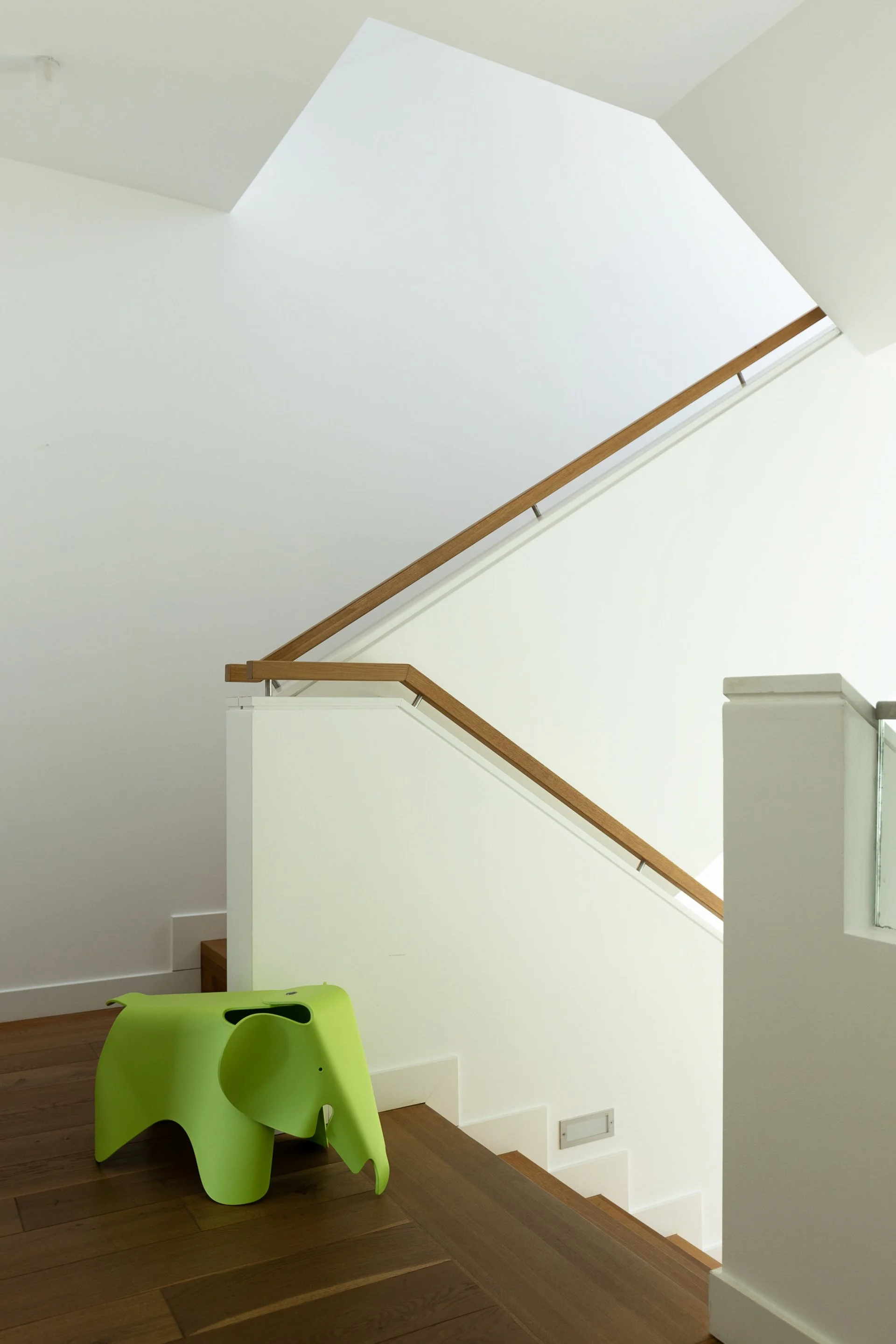 Innenaufnahme eines weißen Hausflurs mit Holztreppe und einem grünen Kindersessel in Form eines Elefanten.