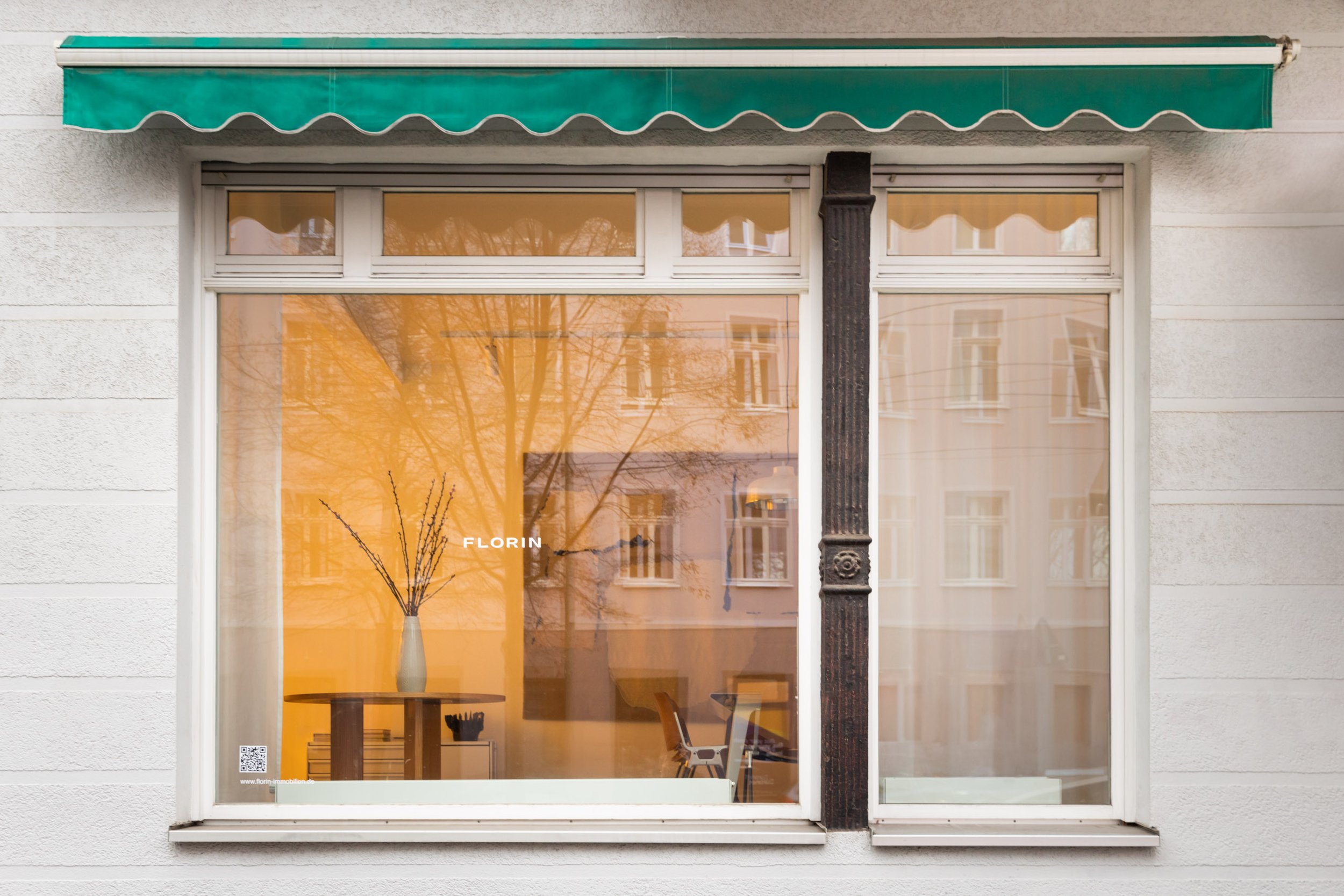 Schaufenster eines des Büros von Florin Immobilien, einem Tisch mit Vase und Zweigen sowie einem Stuhl im Inneren.