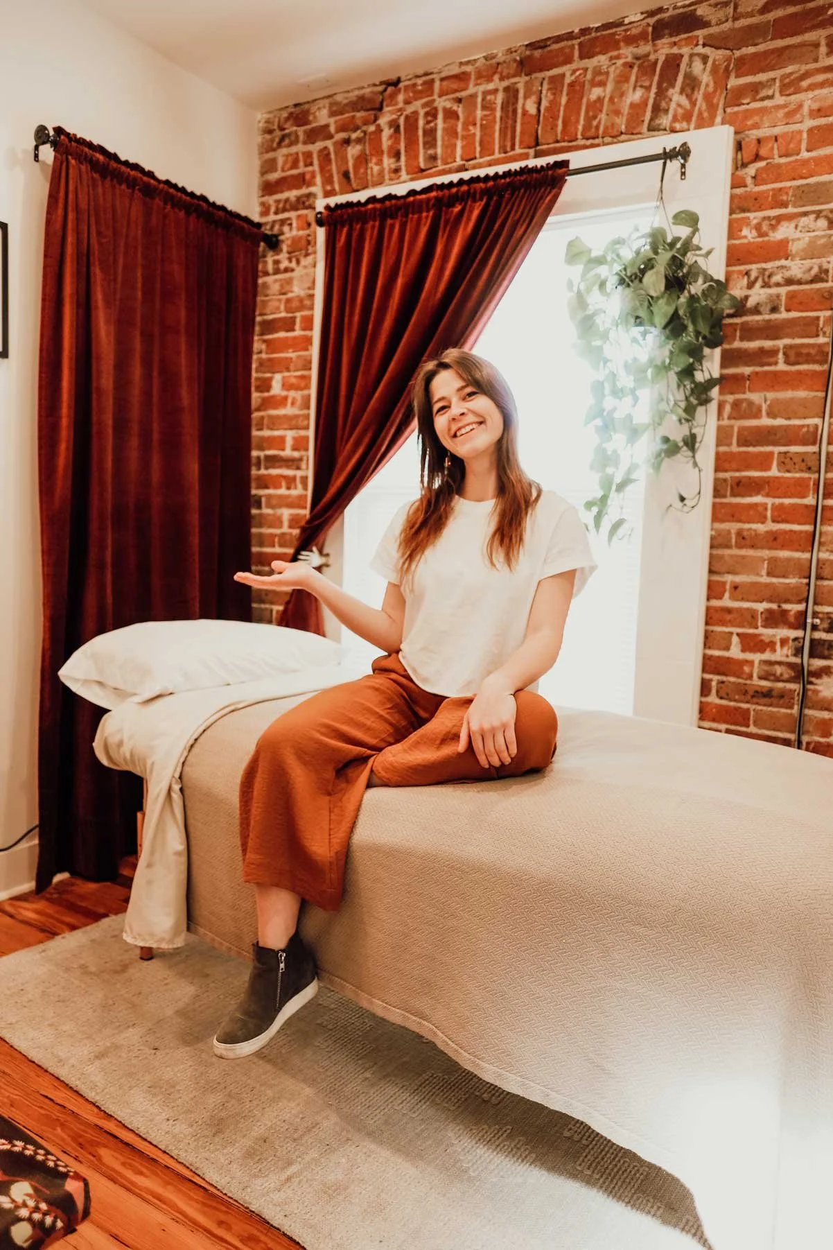 Erin Schemenski sitting, hand open and welcoming, on a Reiki table at The Mindful Bird in Denver, Colorado