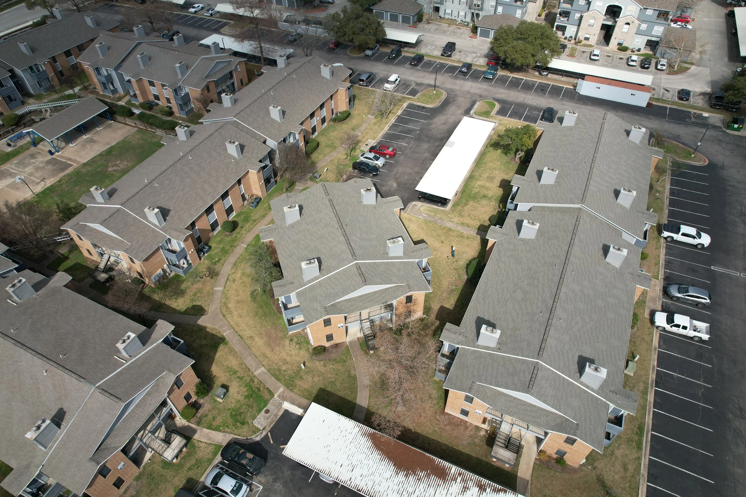 Aerial view of a residential apartment complex with multiple buildings, parking lots, and surrounding pathways.