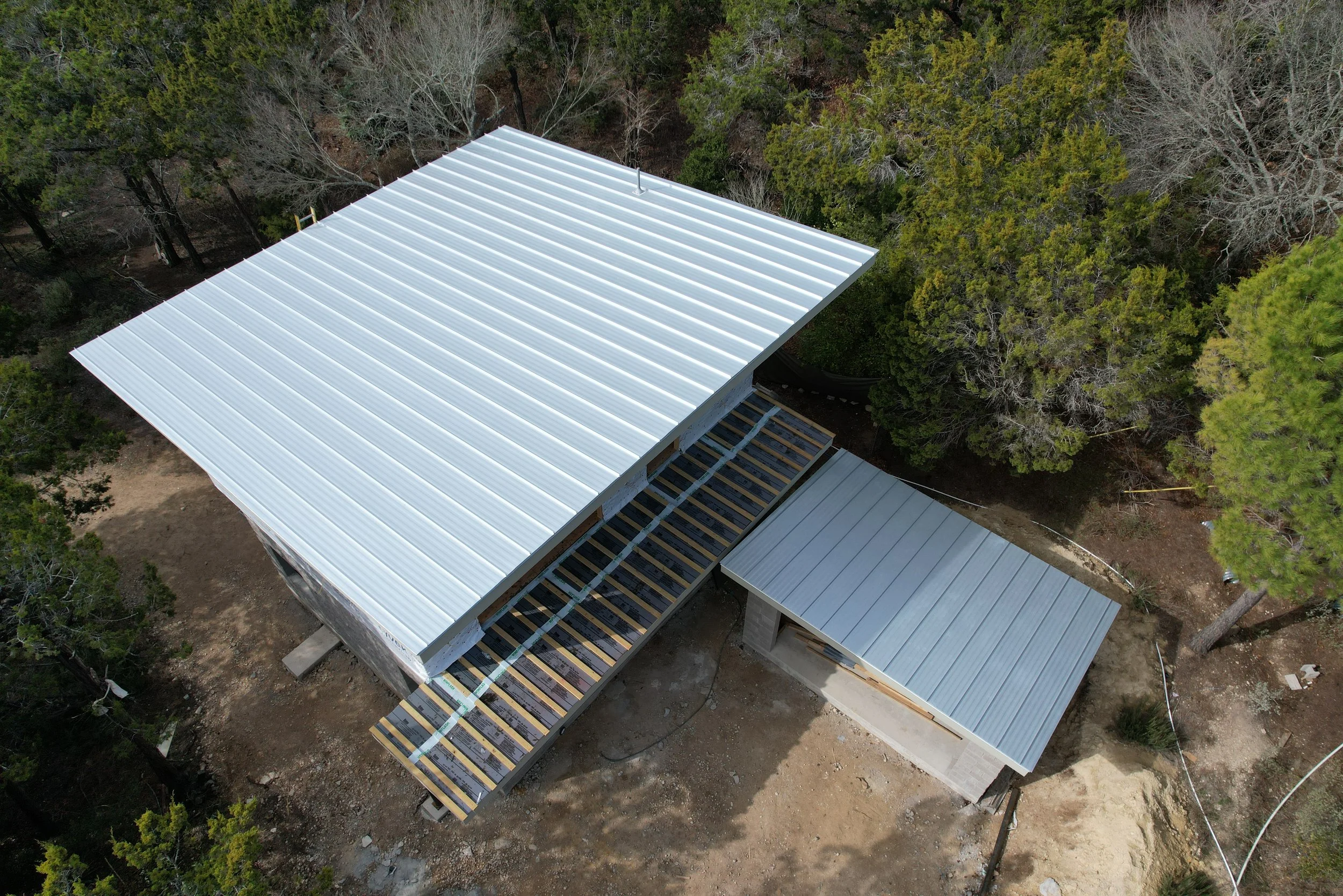 Aerial view of a building under construction with metal roofing surrounded by trees.