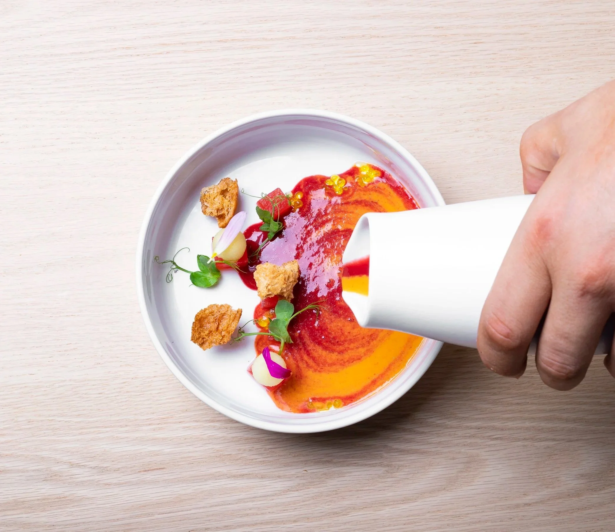 Mesa de comida con diversos platillos, ensalada, vino tinto, y guarniciones en platos de cerámica y porcelana en un ambiente de restaurante