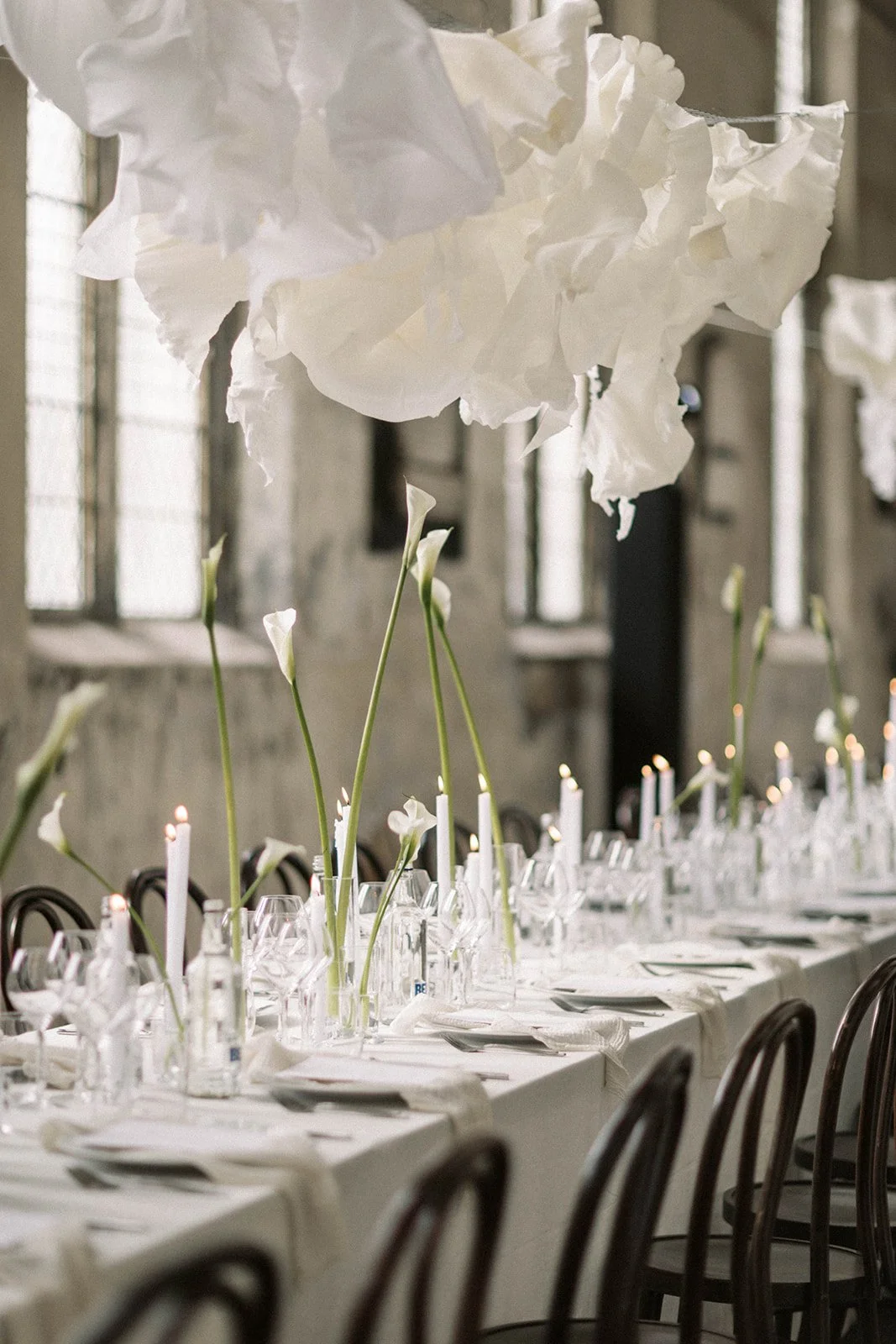 Suspended paper cloud in abandoned church in East London with white Callas and candles across the tables