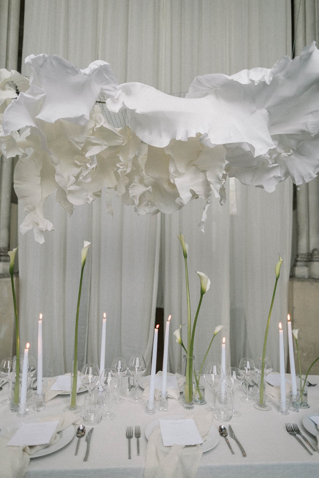 Clouds of sculpted paper suspended over long tables for a large wedding breakfast with Callas and candles