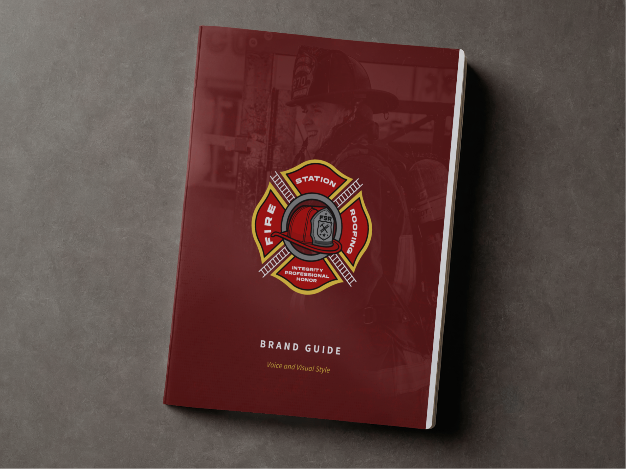 A red fire department brand guide booklet with a firefighter logo on the cover, featuring a helmet and ladder, placed on a gray surface.