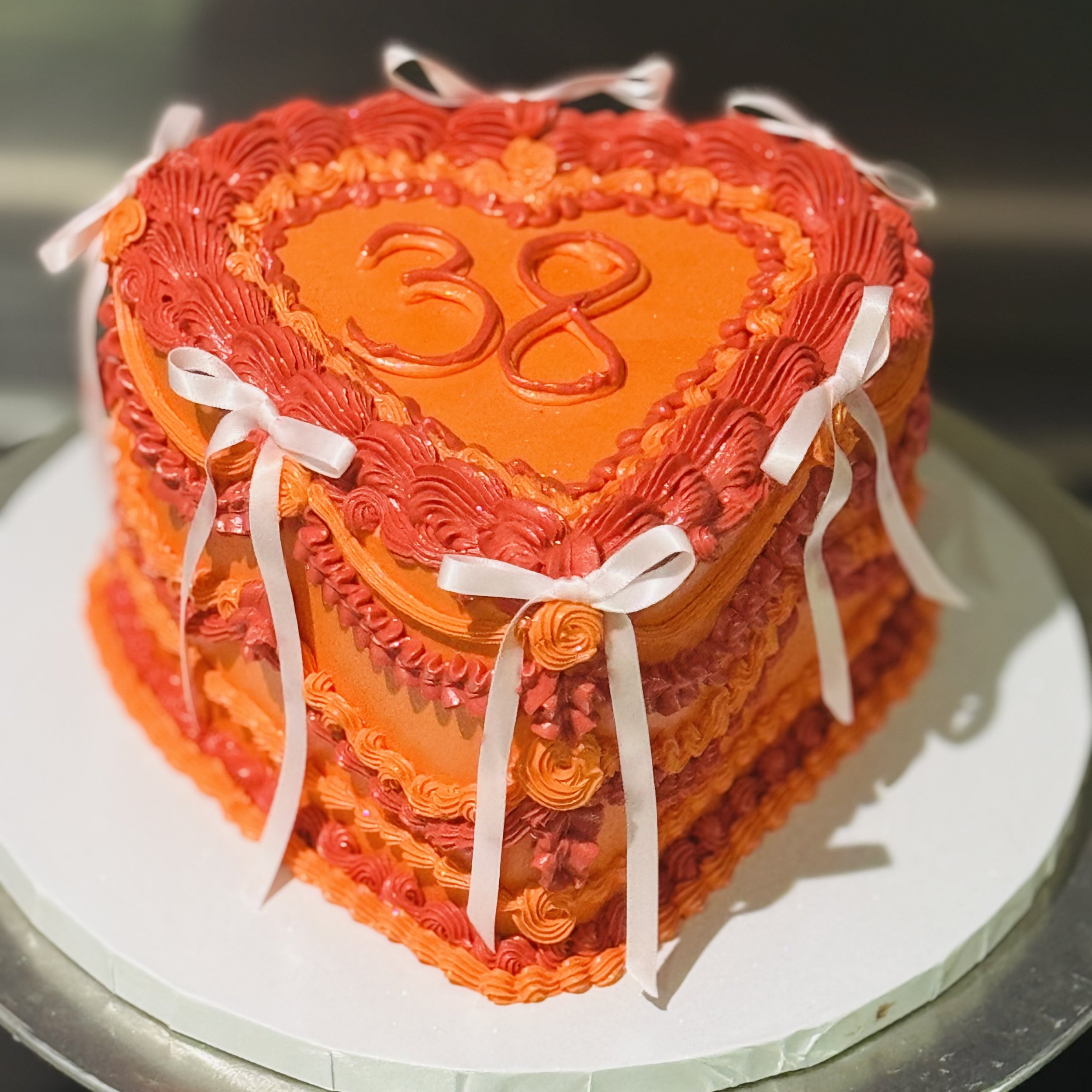 Vintage-style heart-shaped birthday cake in blush pink and ivory, decorated with pearls and ribbons