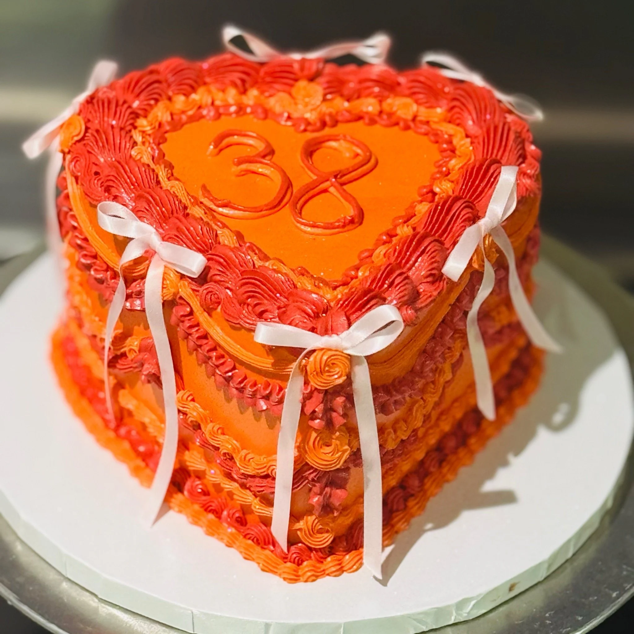 Orange and red vintage heart-shaped 38th birthday cake with bows and decorative piping