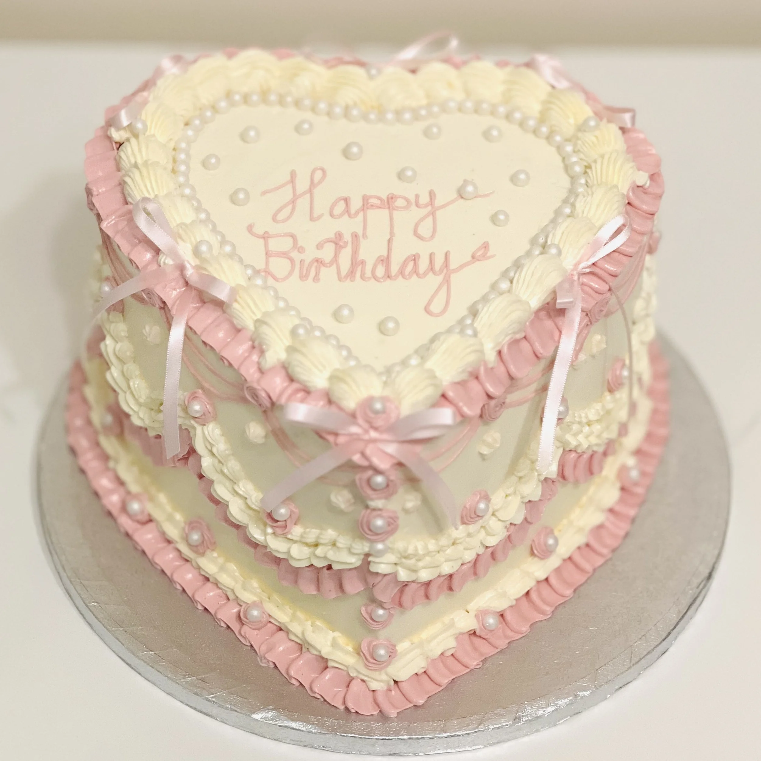 Pink and ivory vintage heart birthday cake with piped buttercream, pearls and bows by BookaCake London