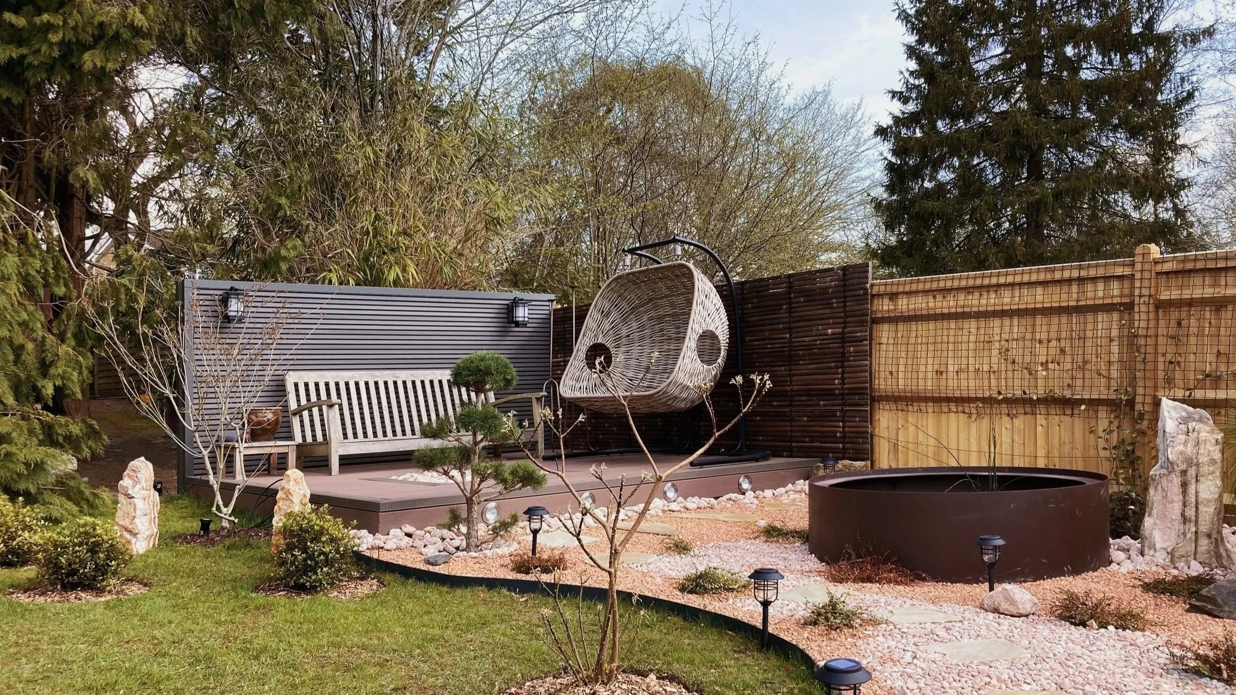 Japanese inspired rear garden designed by Atelier AnK in Kent featuring timber raised terrace, circular water feature, stepping stone pathway and sculptural pine planting