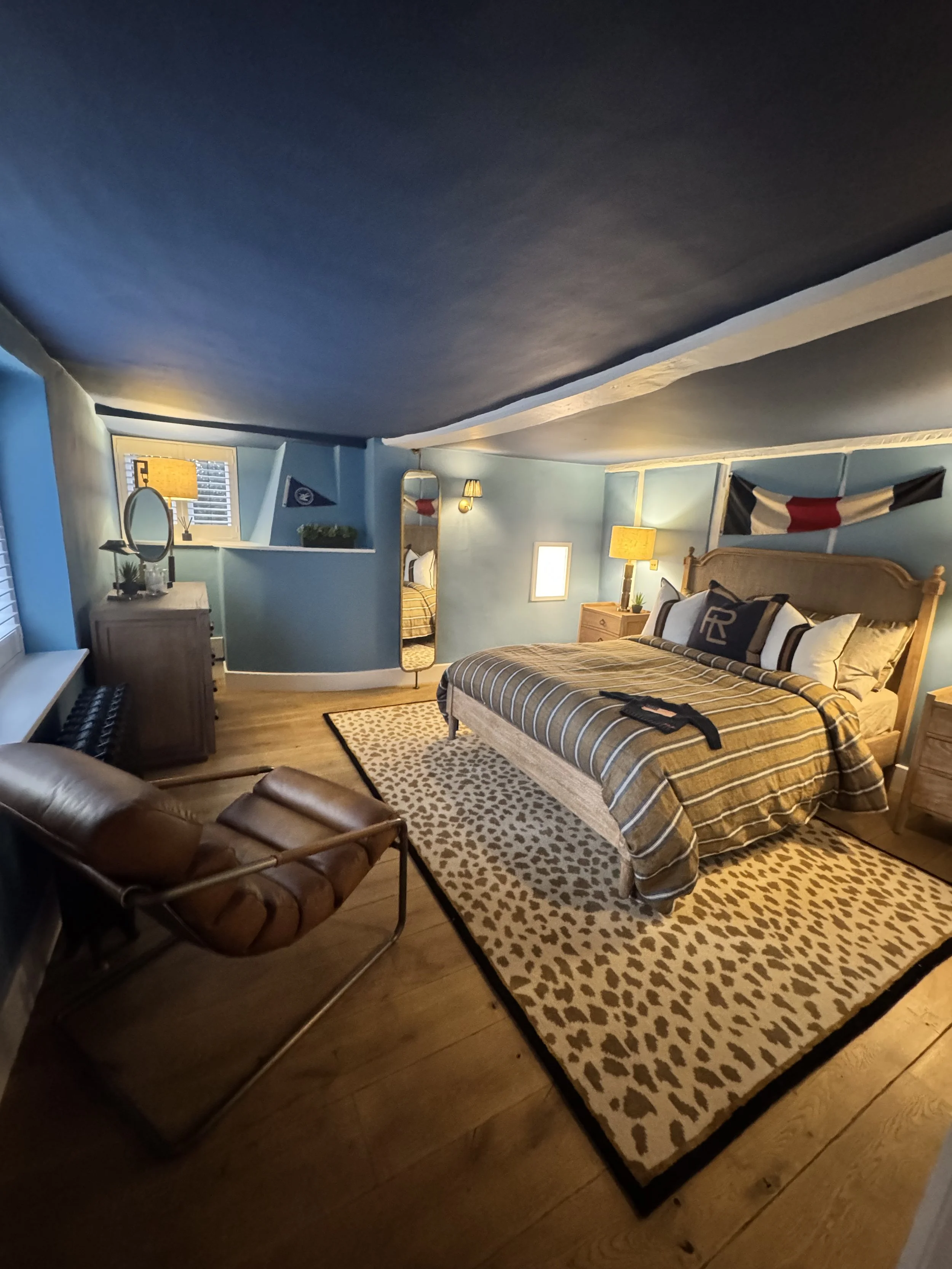 Cosy bedroom with freshly painted blue walls and dark ceiling, featuring wooden furniture, warm lighting, and a neatly styled bed, completed by JN Decorating.