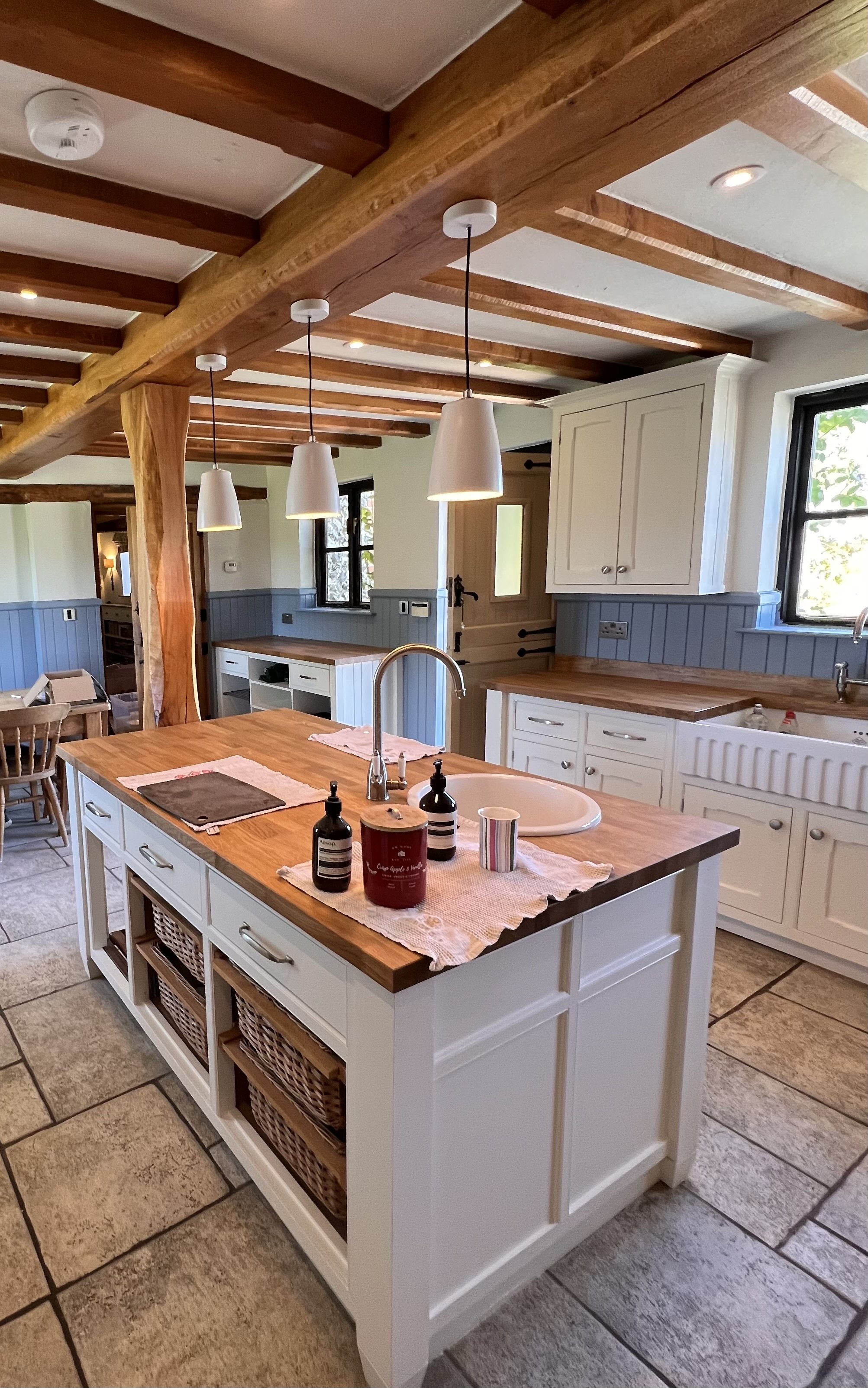 Bright country-style kitchen with freshly painted white cabinetry and blue panelling, wooden worktops, and exposed timber ceiling beams, professionally finished by JN Decorating.