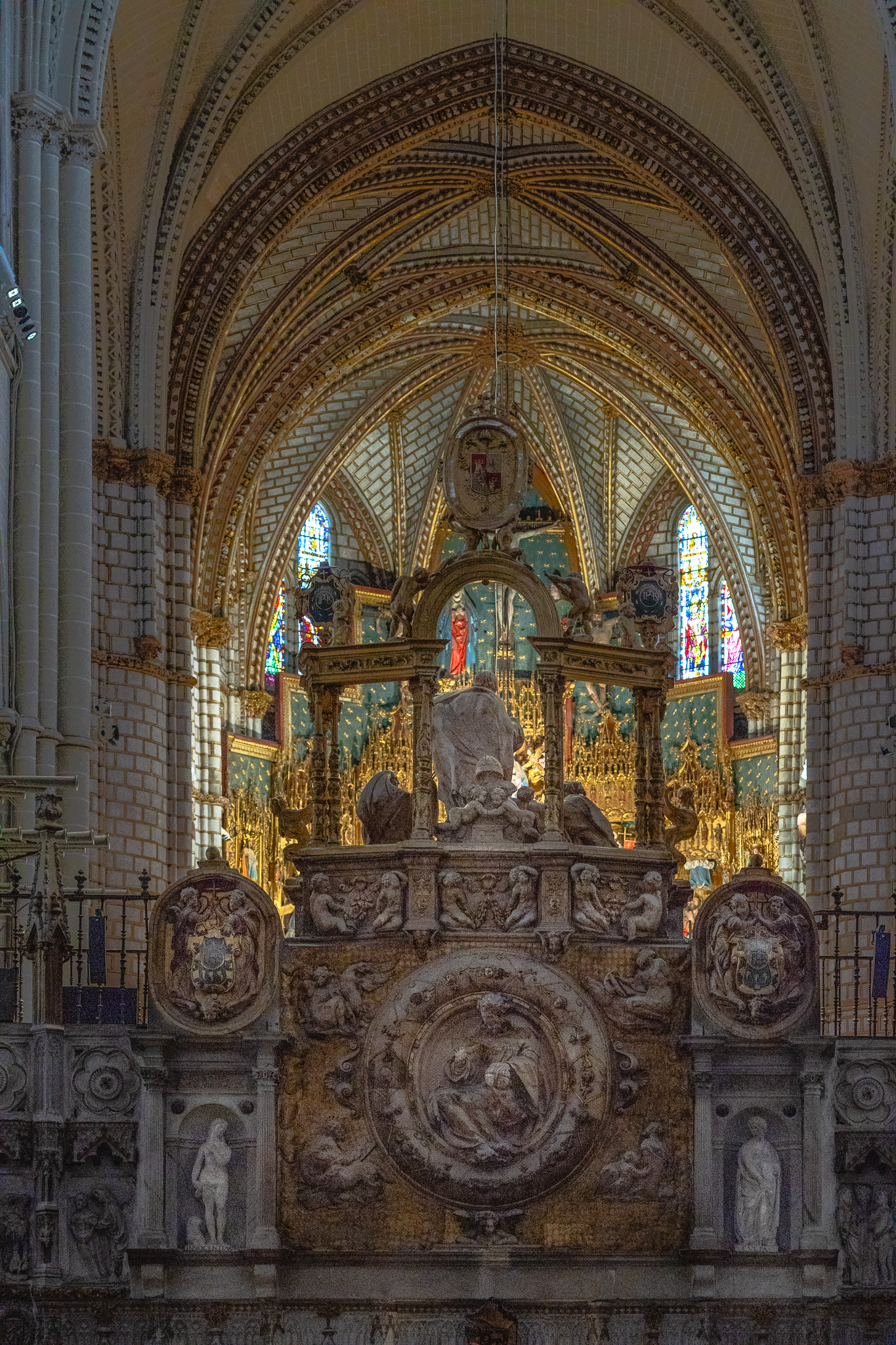 Carved marble and gilt screen at the rear of the choir enclosure in Toledo Cathedral, beneath a ribbed star vault, with stained glass windows on either flank